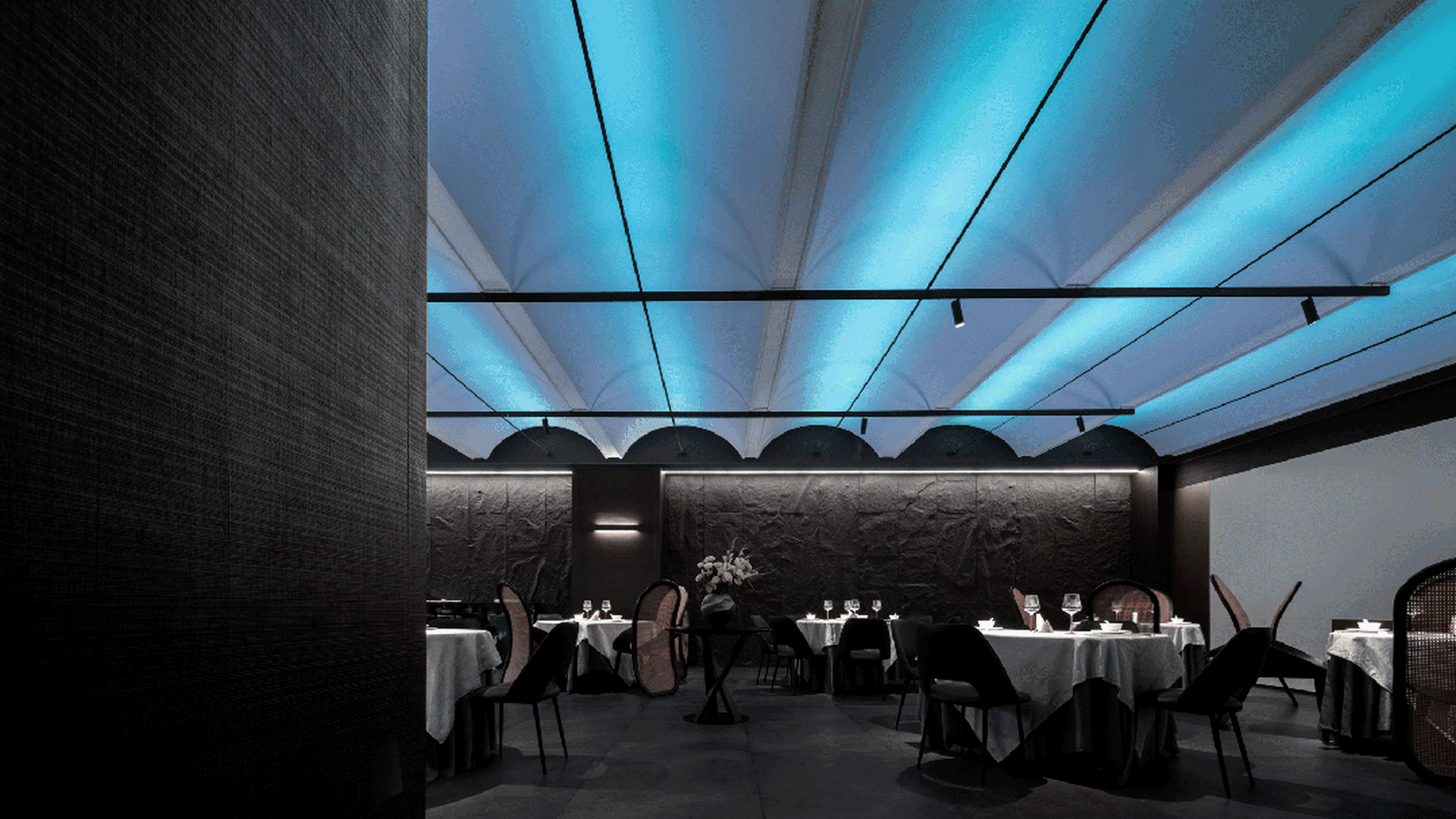 A modern restaurant with black metallic accents and blue lighting features a geometric pattern on the ceiling and black tiles