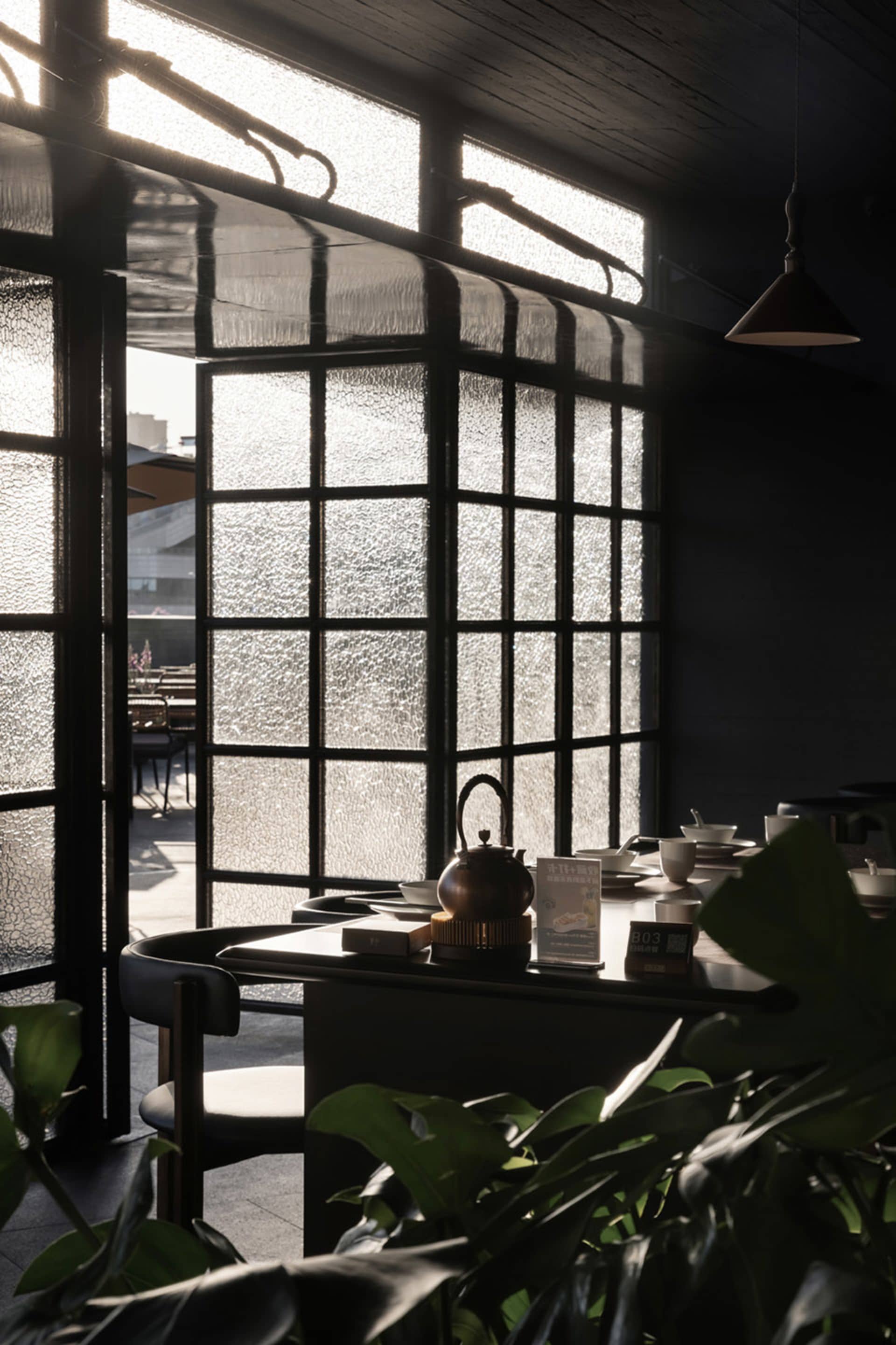 Interior view of an industrial-style restaurant with glass walls, wooden tables, and metal accents.