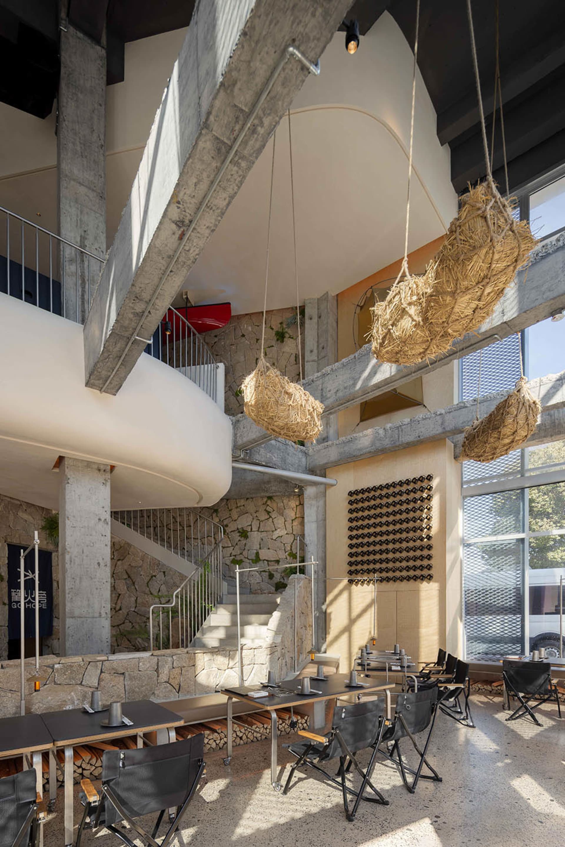 Modern industrial restaurant featuring concrete and stone walls, wooden tables, woven hanging baskets, and exposed concrete b