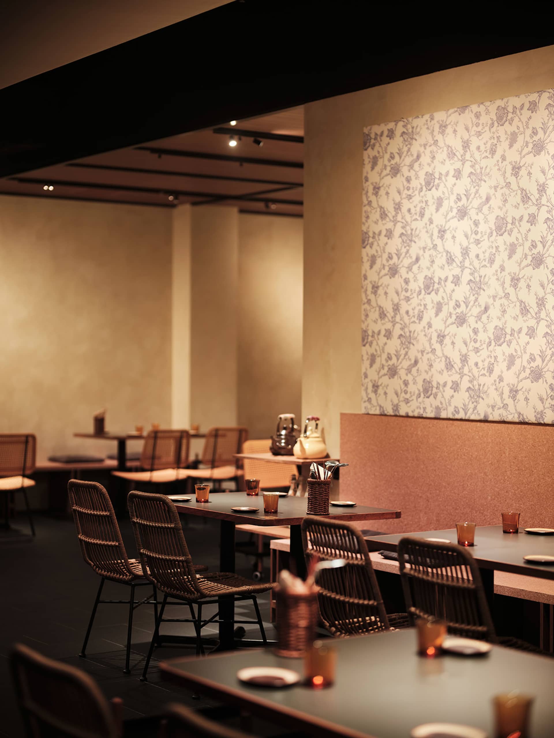 Interior view of a restaurant showcasing wooden tables, fabric chairs, and floral wallpaper.