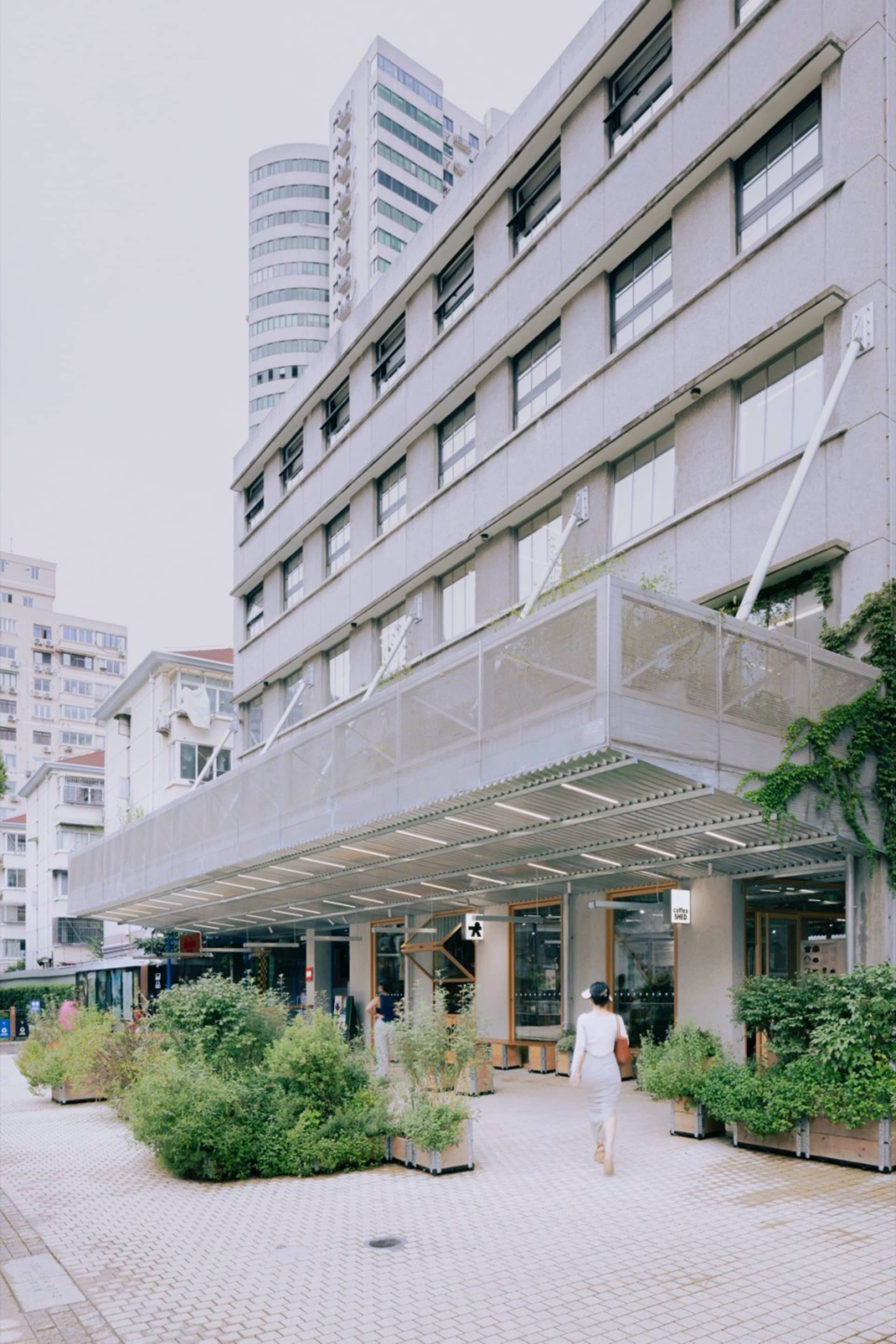 都市零售店面,混凝土外牆、玻璃展示窗與綠意植栽花盆。