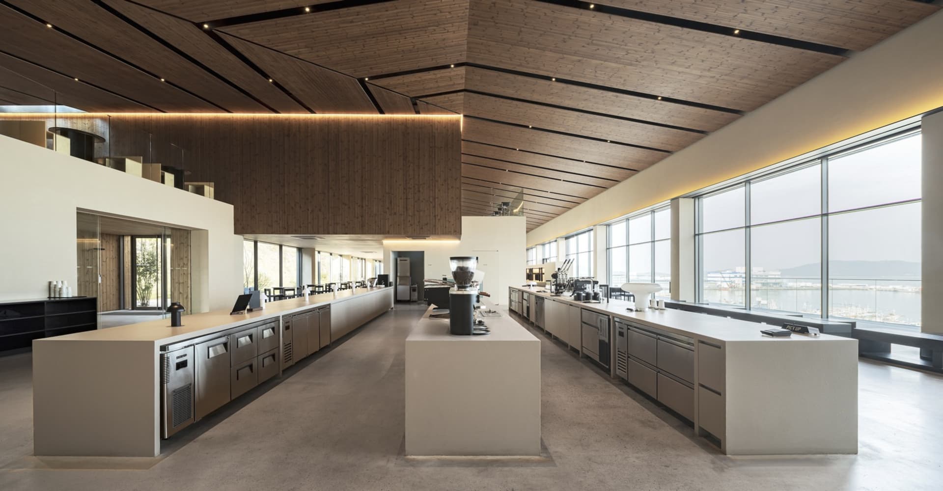 A spacious, industrial-style commercial kitchen with concrete countertops, steel appliances, and large windows.