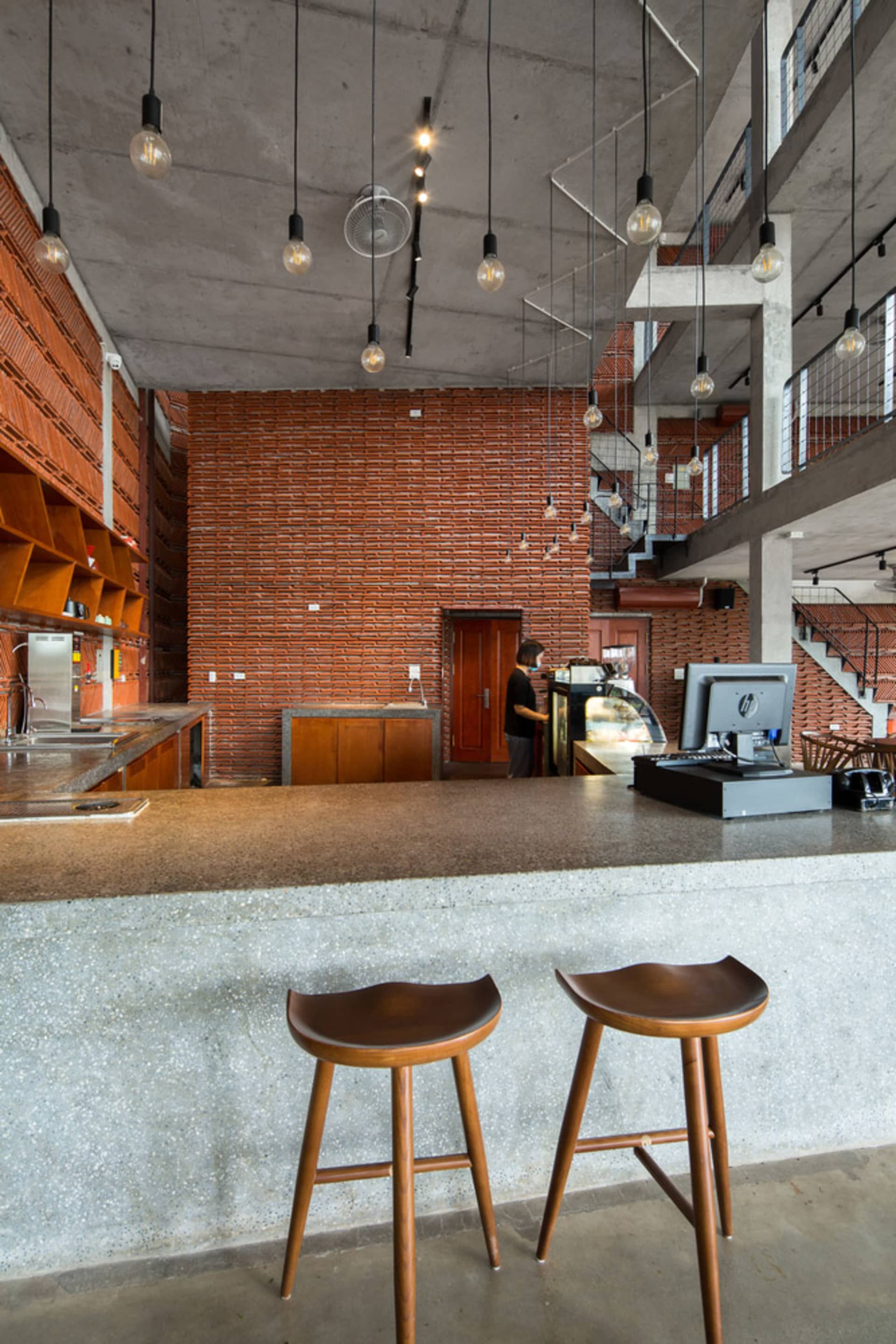 An industrial-style café interior featuring a brick wall counter with concrete flooring and hanging light bulbs.