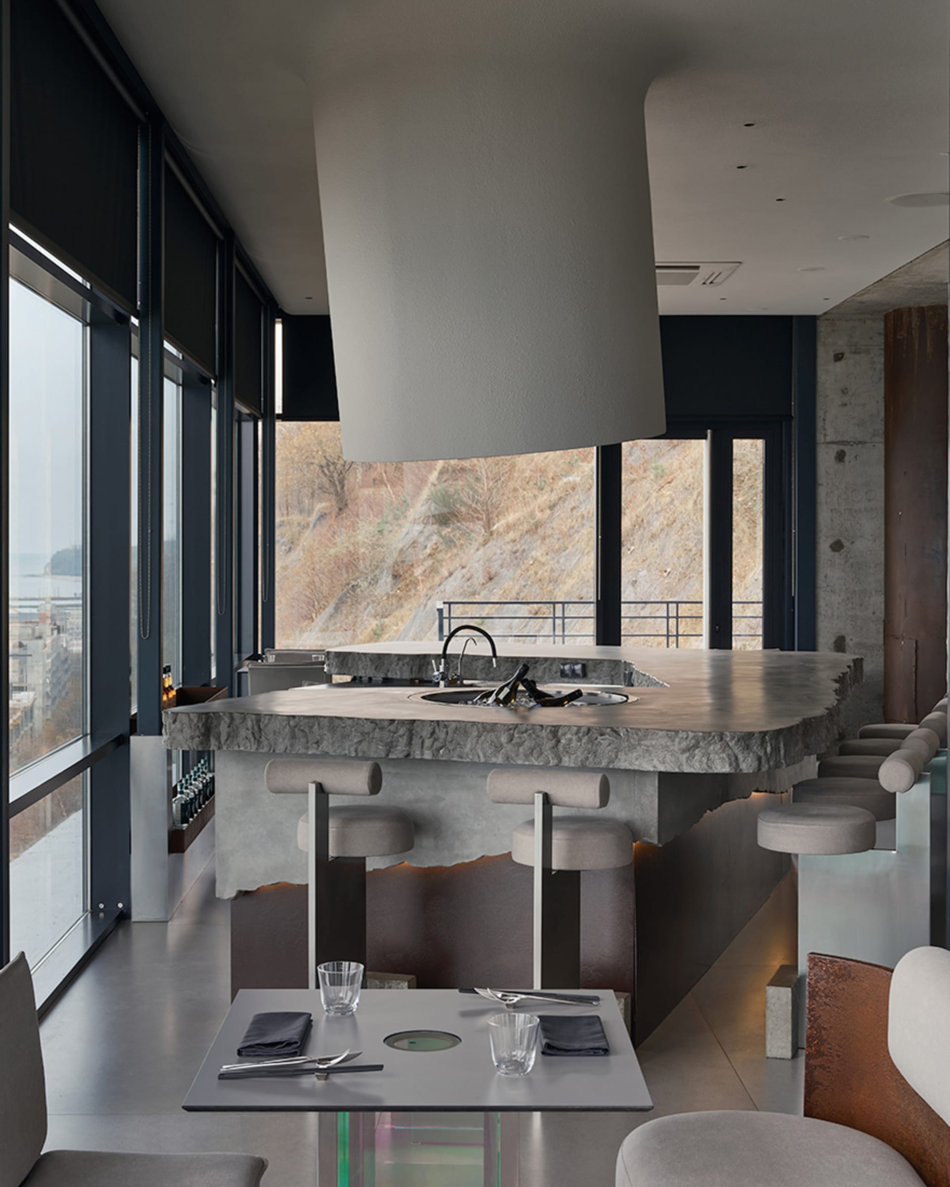 A modern industrial restaurant with a concrete counter, stools, and table setting.