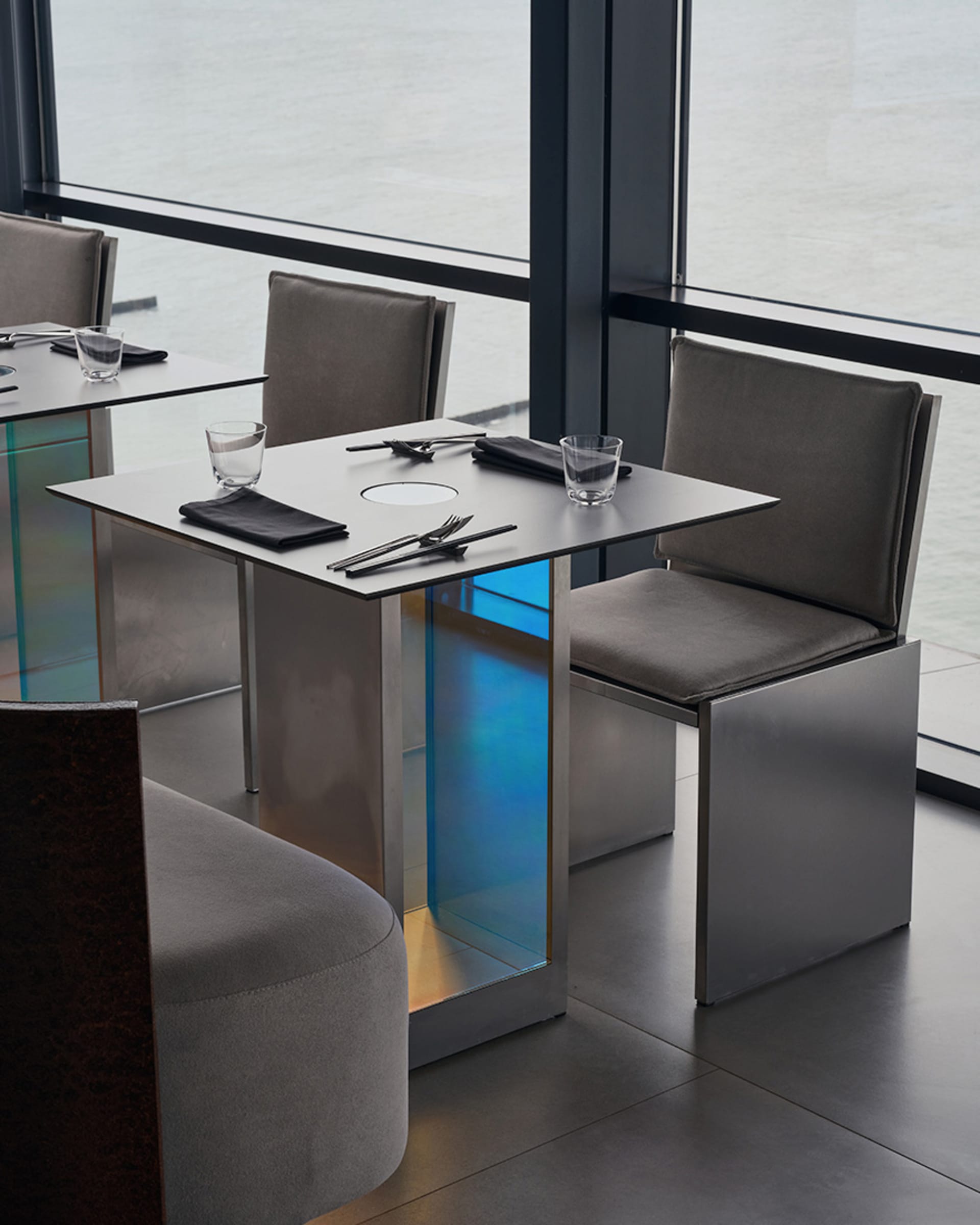 A modern restaurant with sleek metal and glass furniture and a waterfront view.