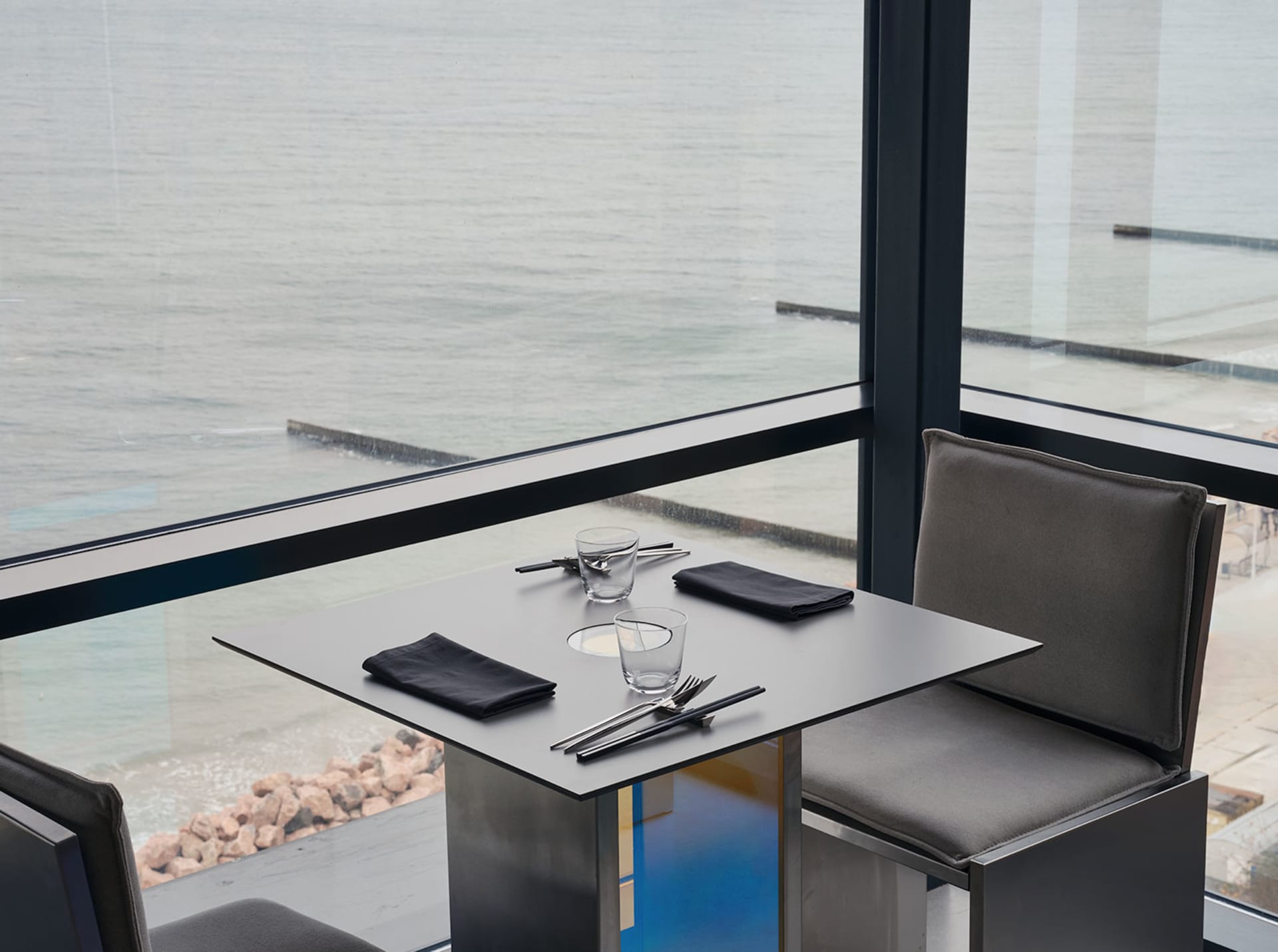 Modern restaurant setting with a metal table, leather chairs, and a stunning sea view.