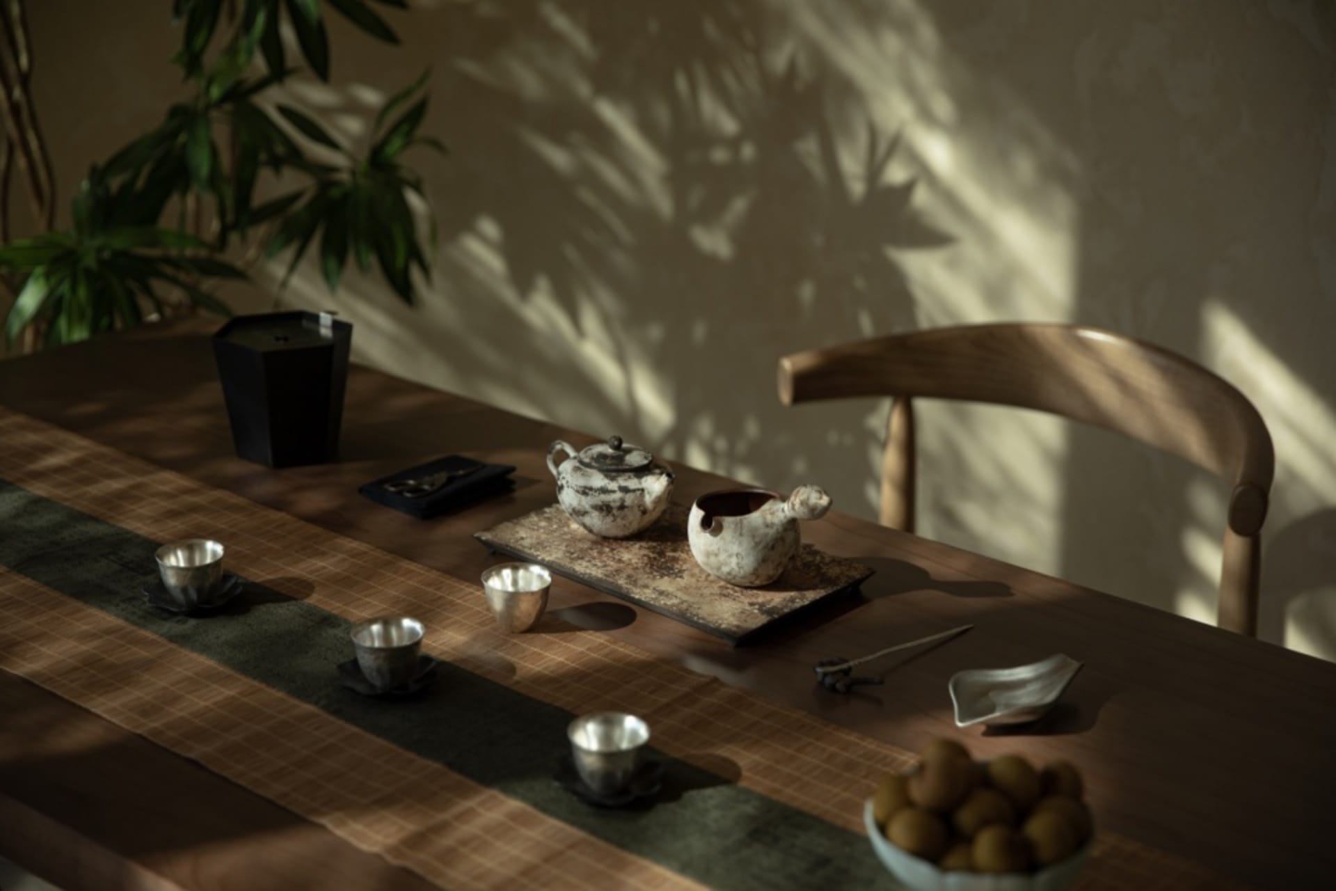 A wooden table with ceramic tea pots and cups, surrounded by greenery and natural light.