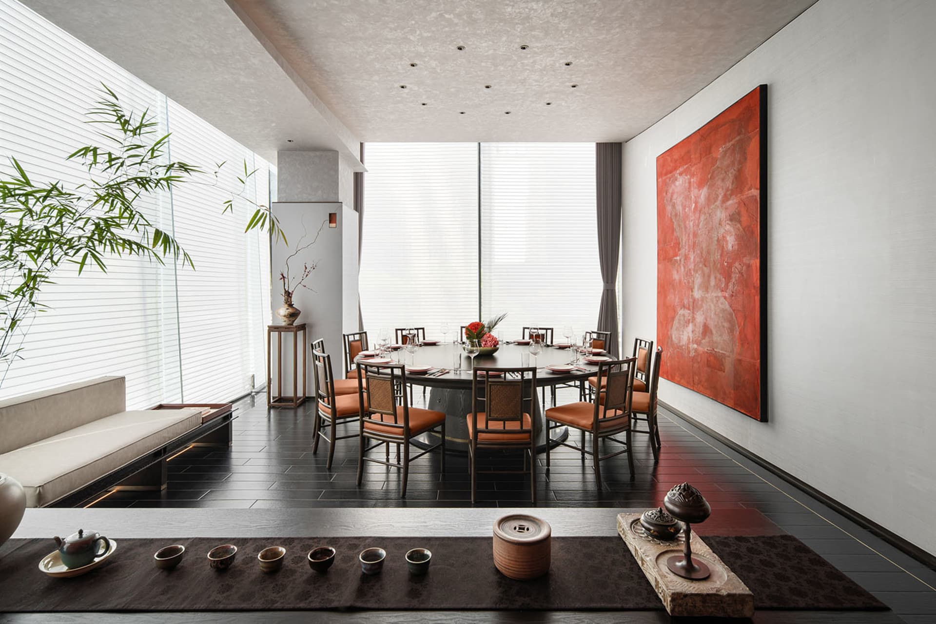 A modern dining room with a large round table surrounded by chairs, set with plates, cutlery, and flowers. The room features 