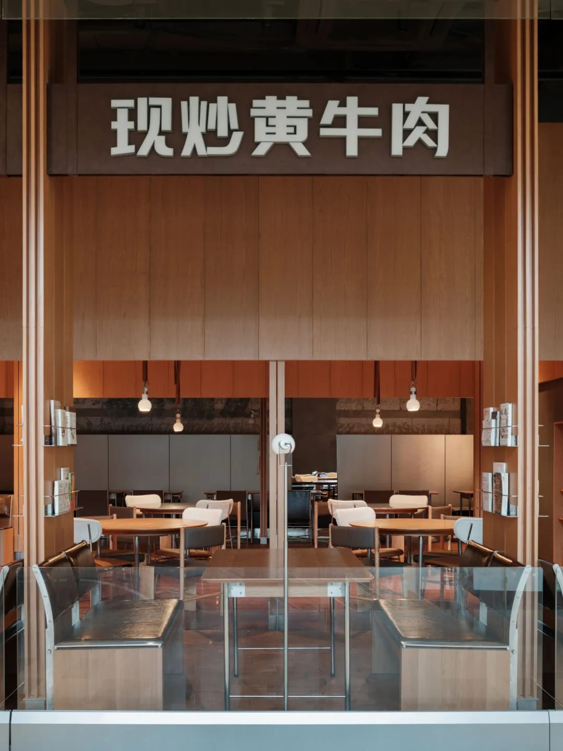 Modern restaurant interior with wooden tables, white chairs, and glass partitions.