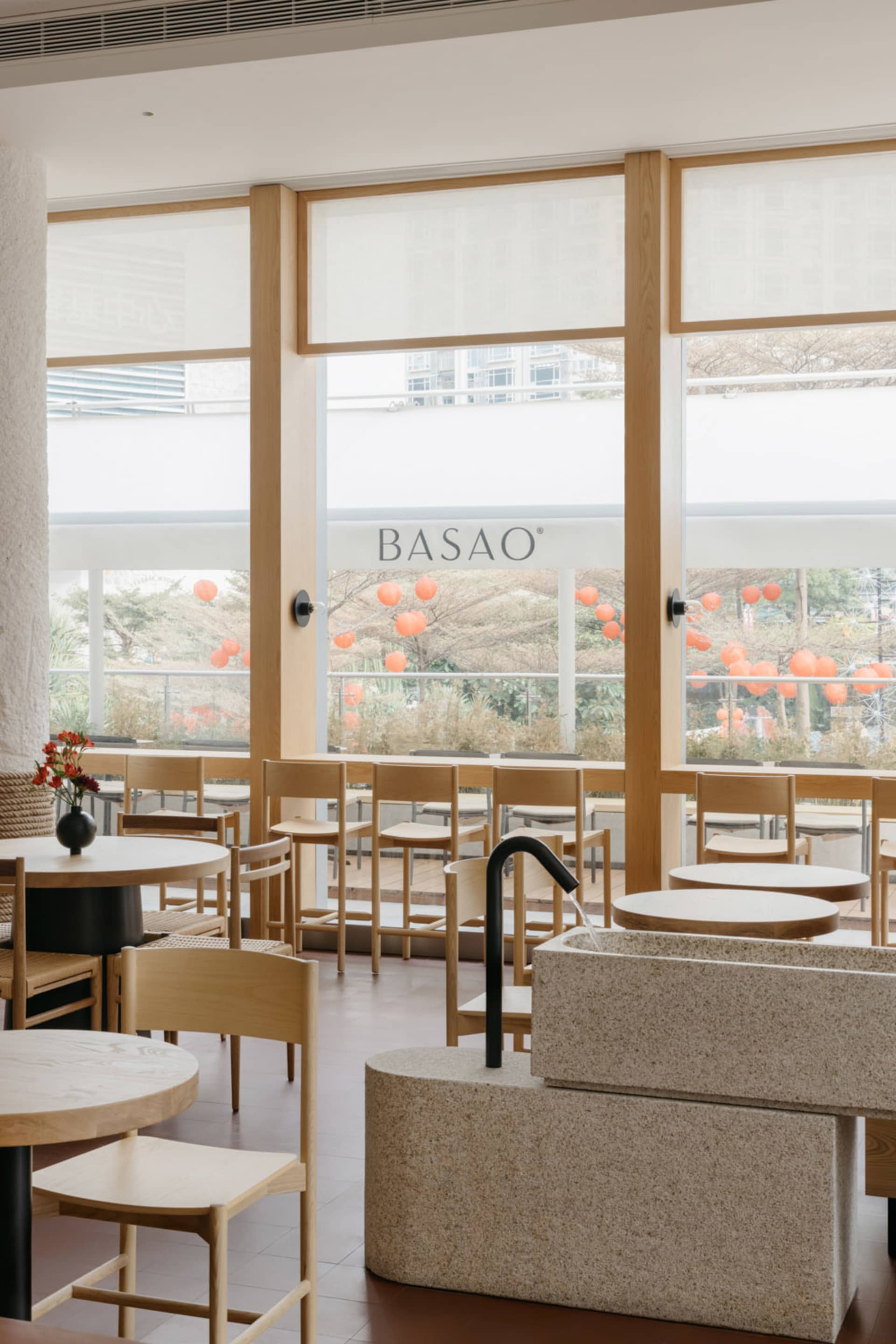 Contemporary restaurant interior featuring wooden tables and chairs, stone sink, and minimalist design.