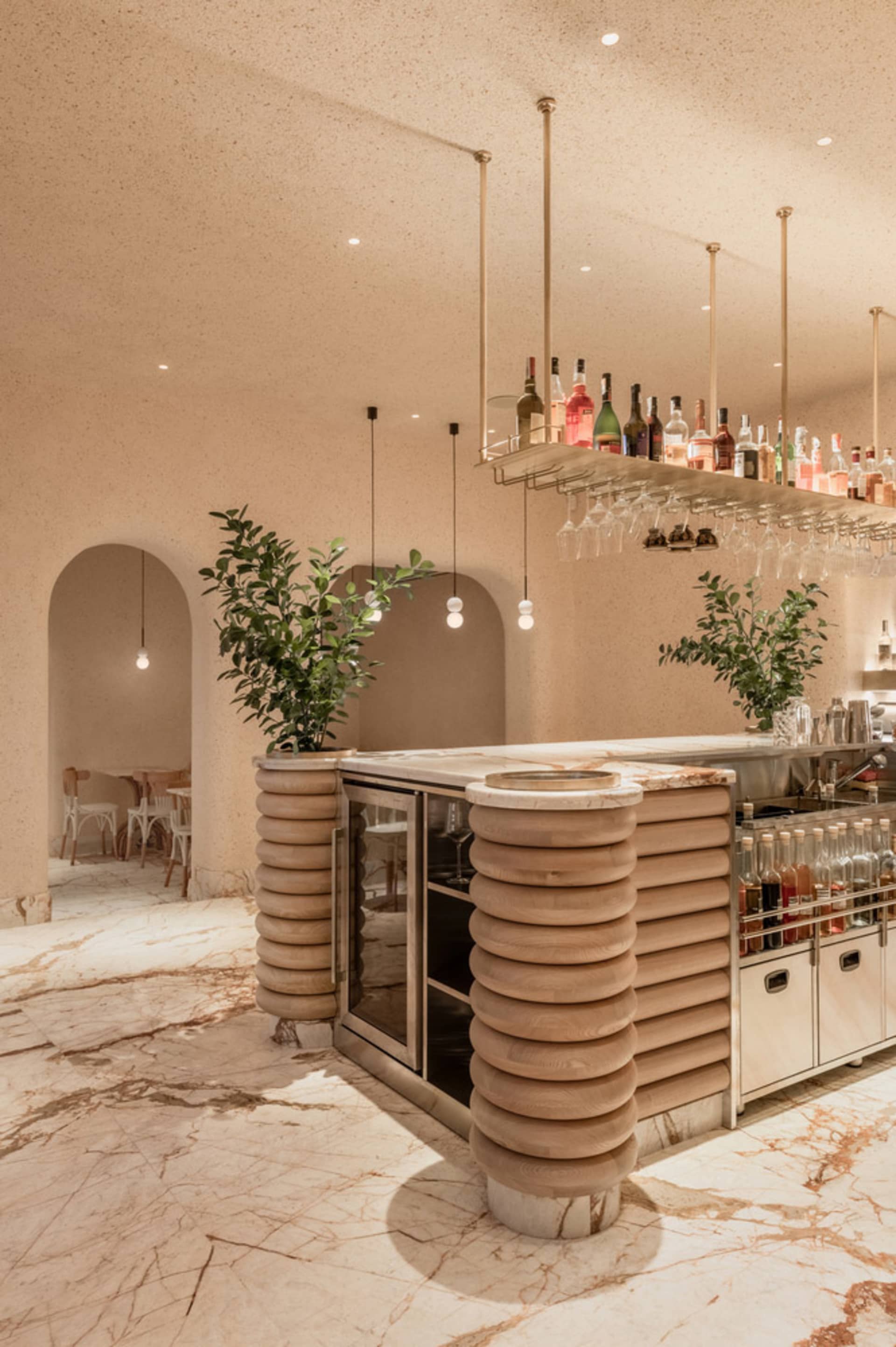 A modern bar area with a wooden counter, marble floor, and hanging wine bottles.