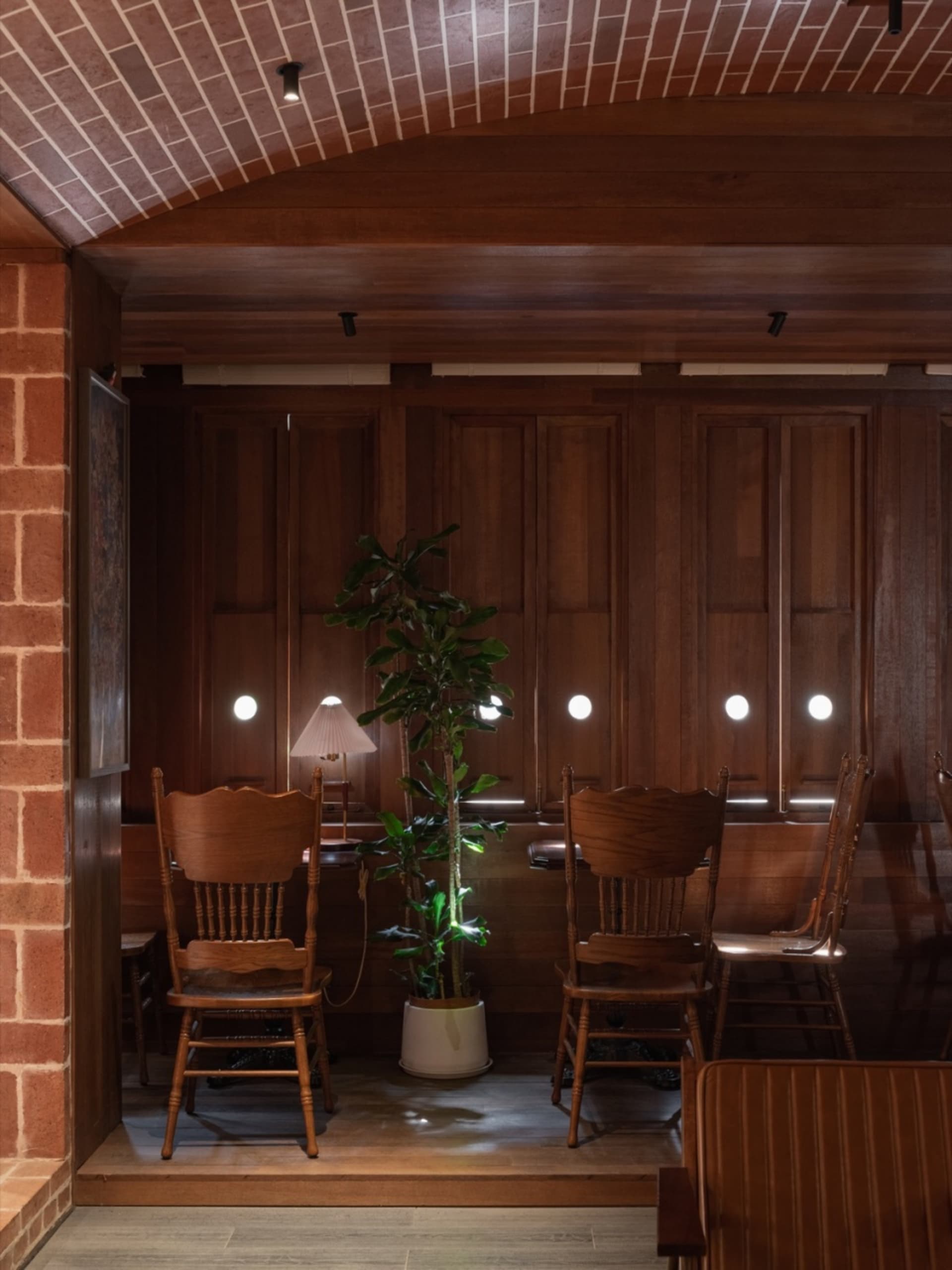 Industrial-style cafe interior with wooden furniture, a potted plant, and wall-mounted lights.