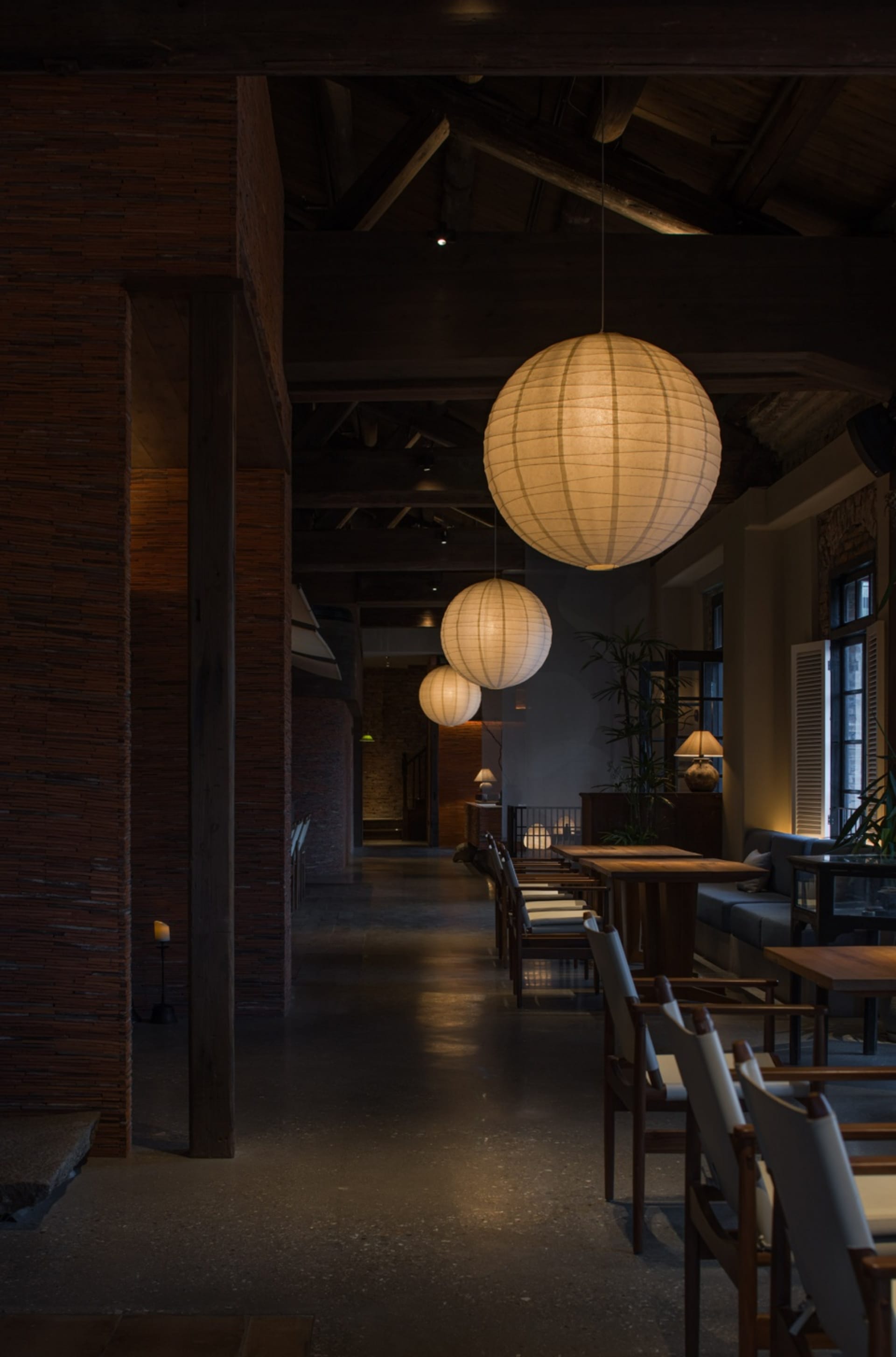 Industrial-style restaurant interior featuring hanging paper lanterns, wooden seating, and concrete flooring.