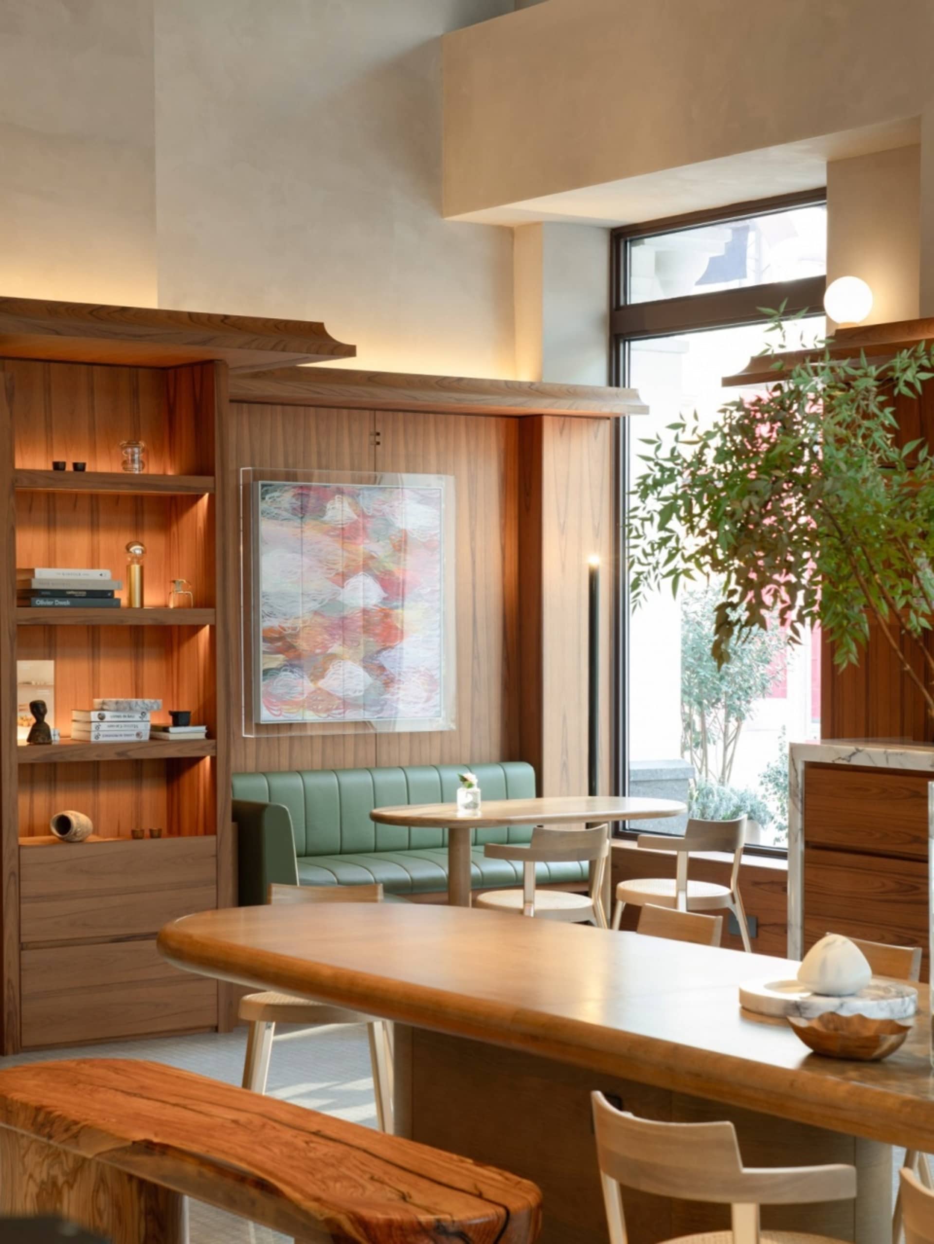 A modern restaurant interior with wooden furniture, green seating, and a large potted plant.