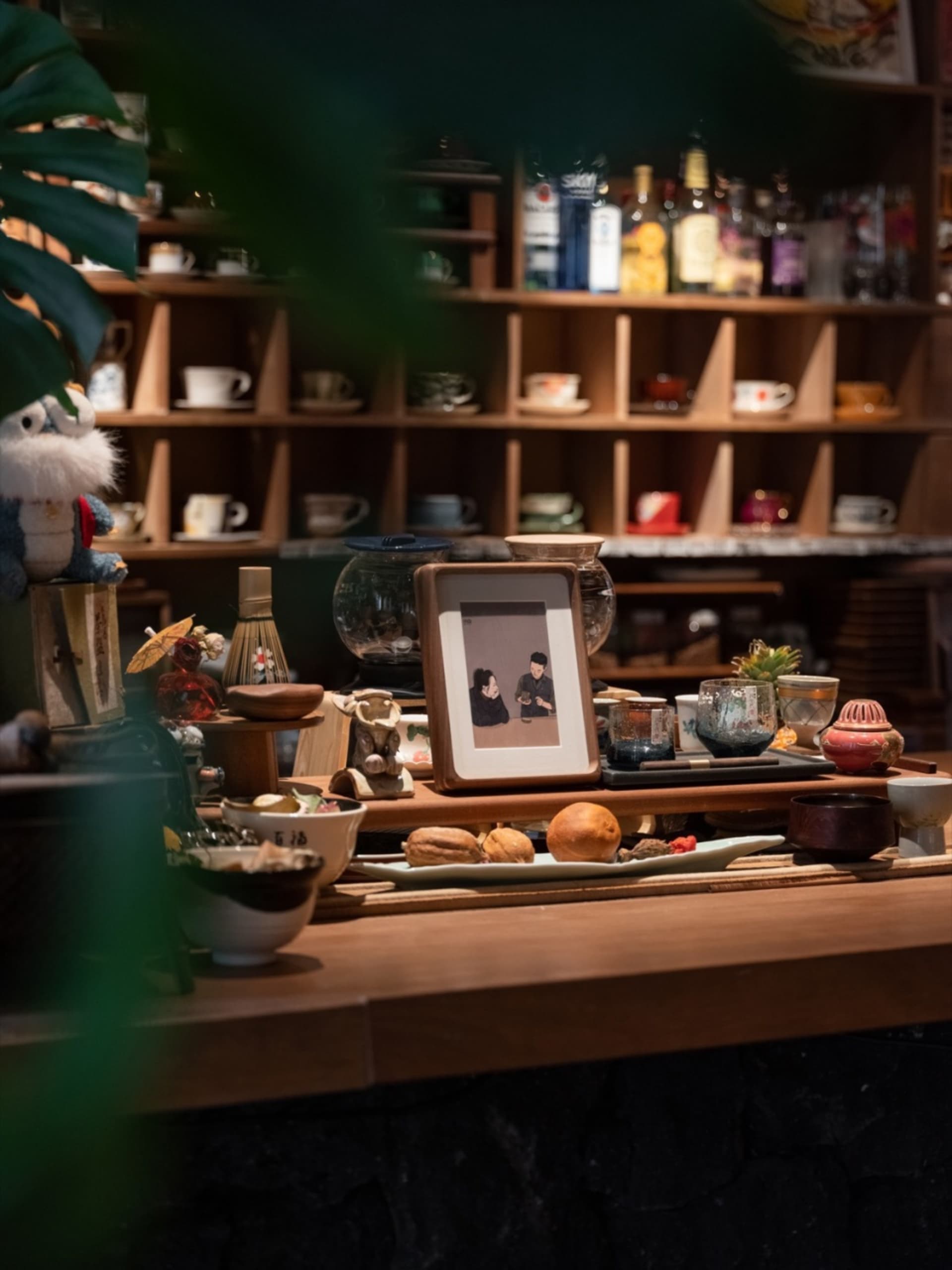 溫馨的咖啡廳場景,展示架上陳列陶瓷與木製物品,搭配兩人肖像畫框,以及各式咖啡相關用品。