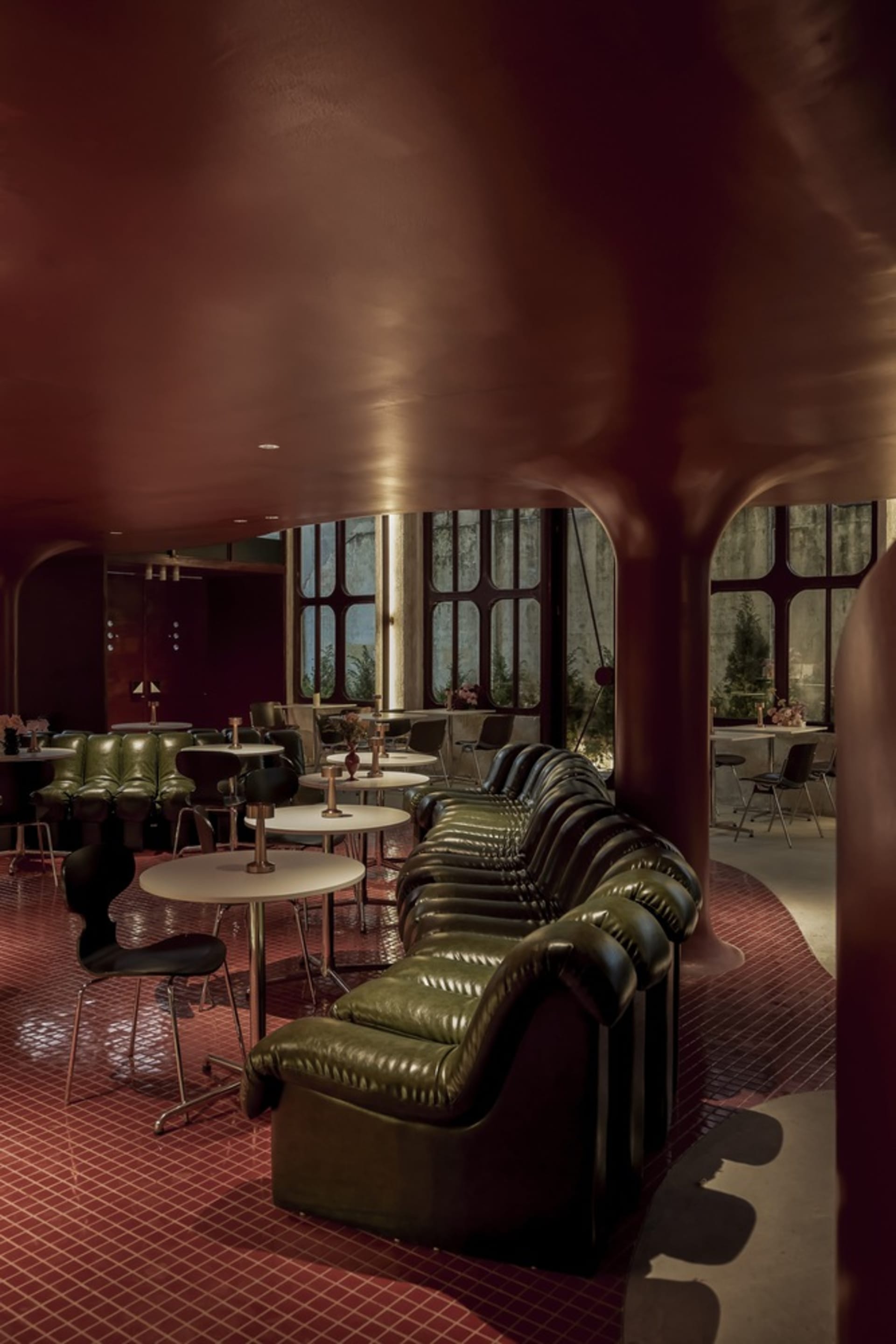 A sleek, modern industrial restaurant bar featuring green leather sofas and black metal furniture.
