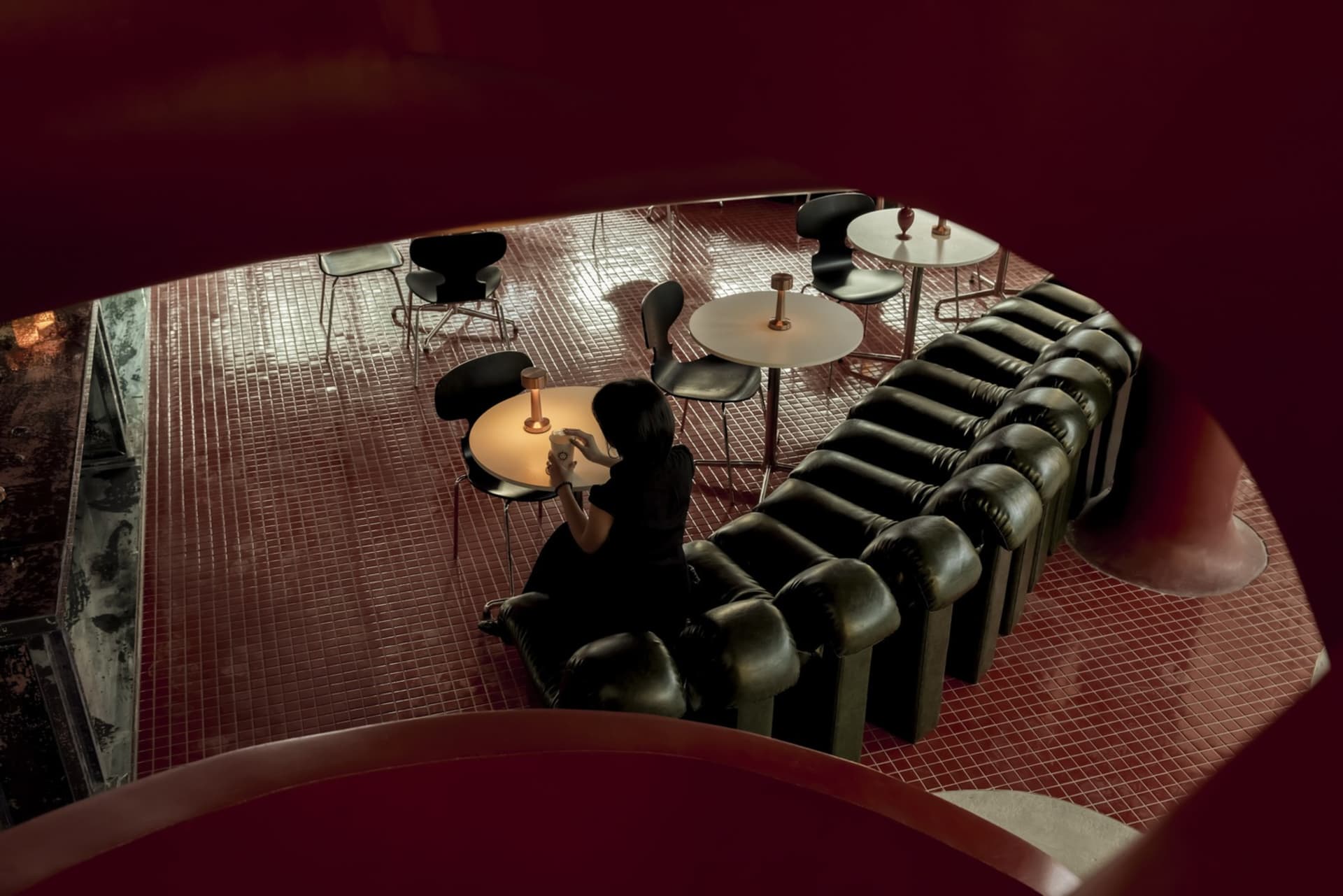 A modern cafeteria with black leather furniture and a metal floor, featuring a person sitting at a table with a drink.