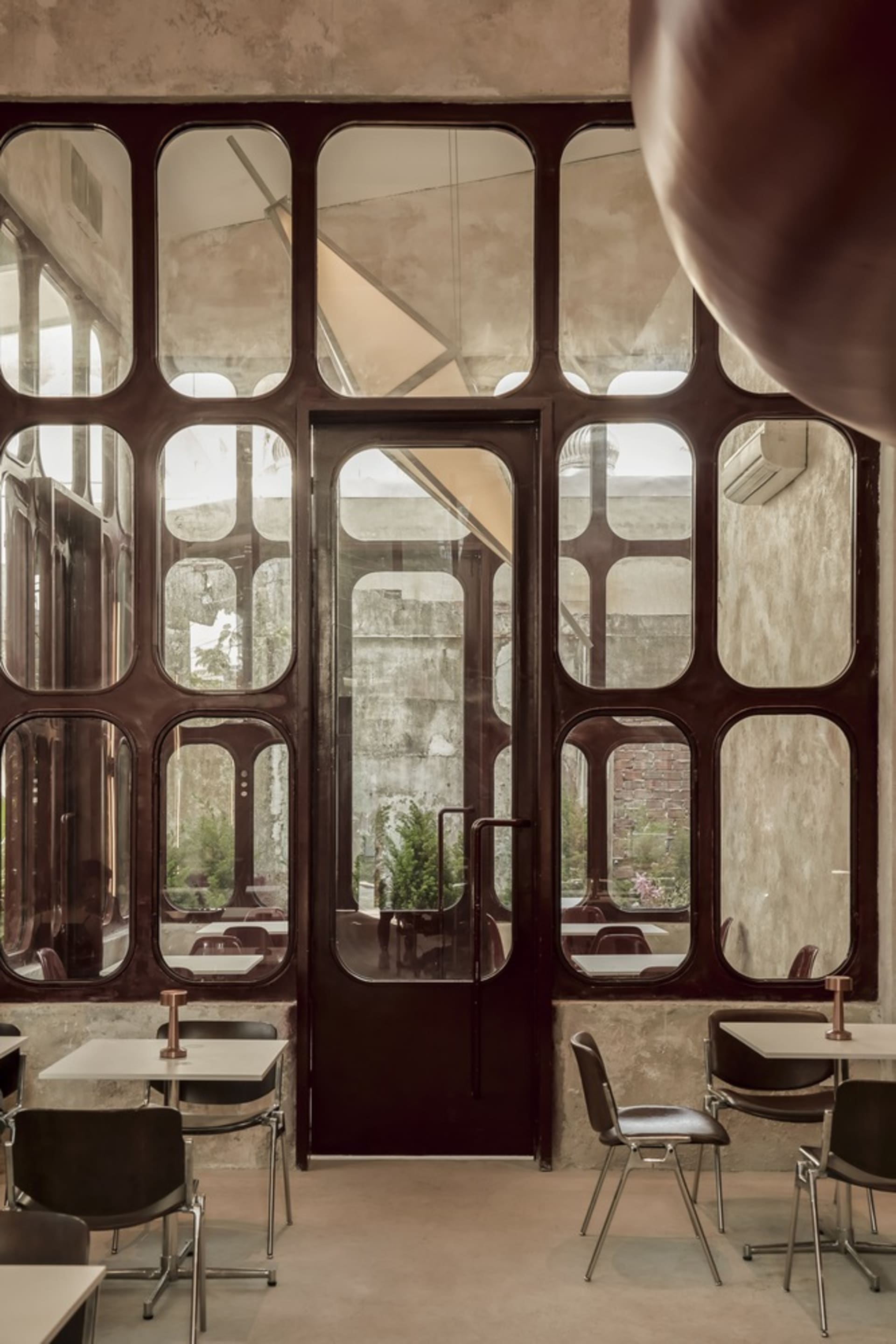 A modern industrial restaurant interior with metal-frame windows, glass panels, and concrete walls and floors.