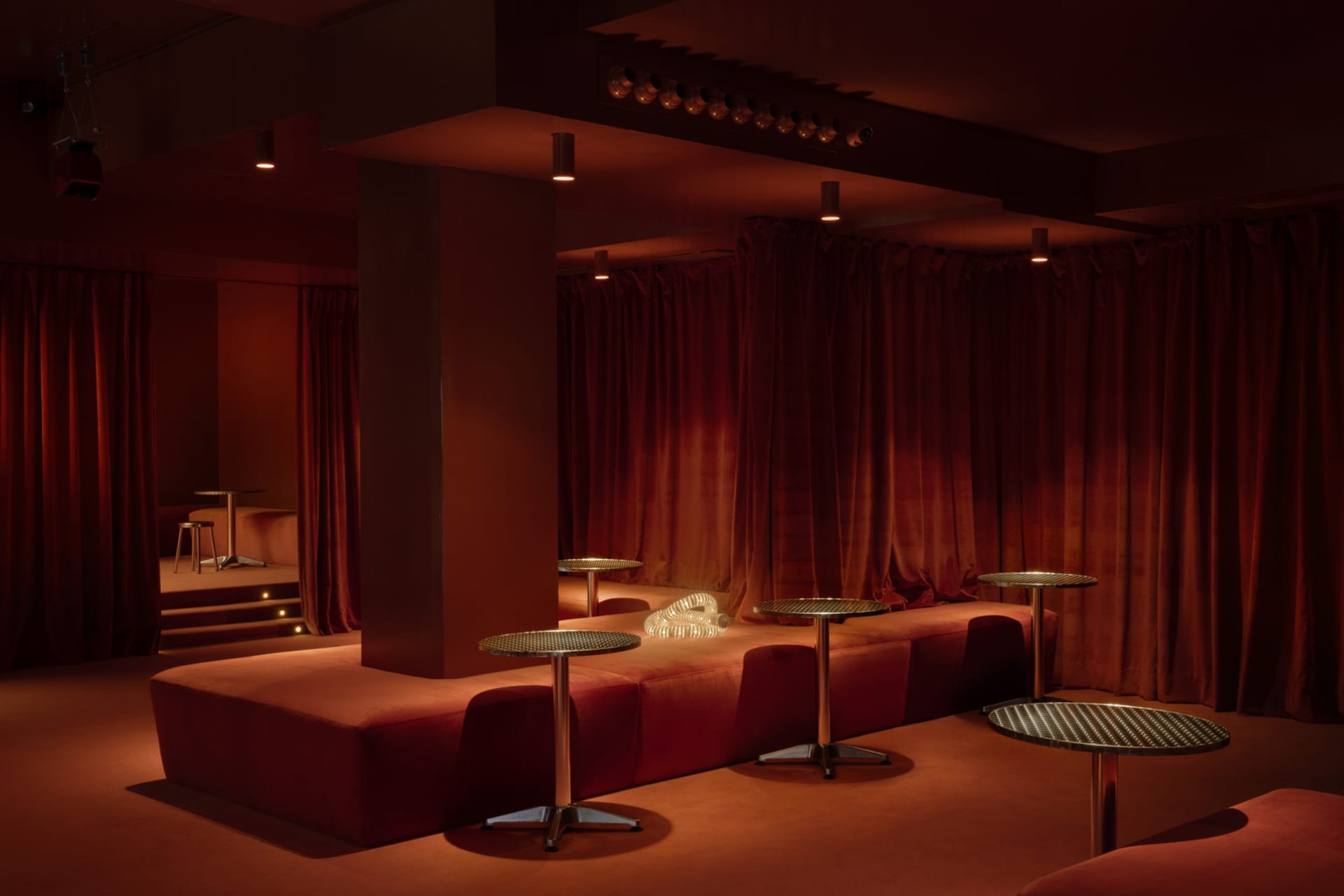 A modern nightclub interior featuring plush red velvet seating and illuminated tables, with a focus on the luxurious and eleg