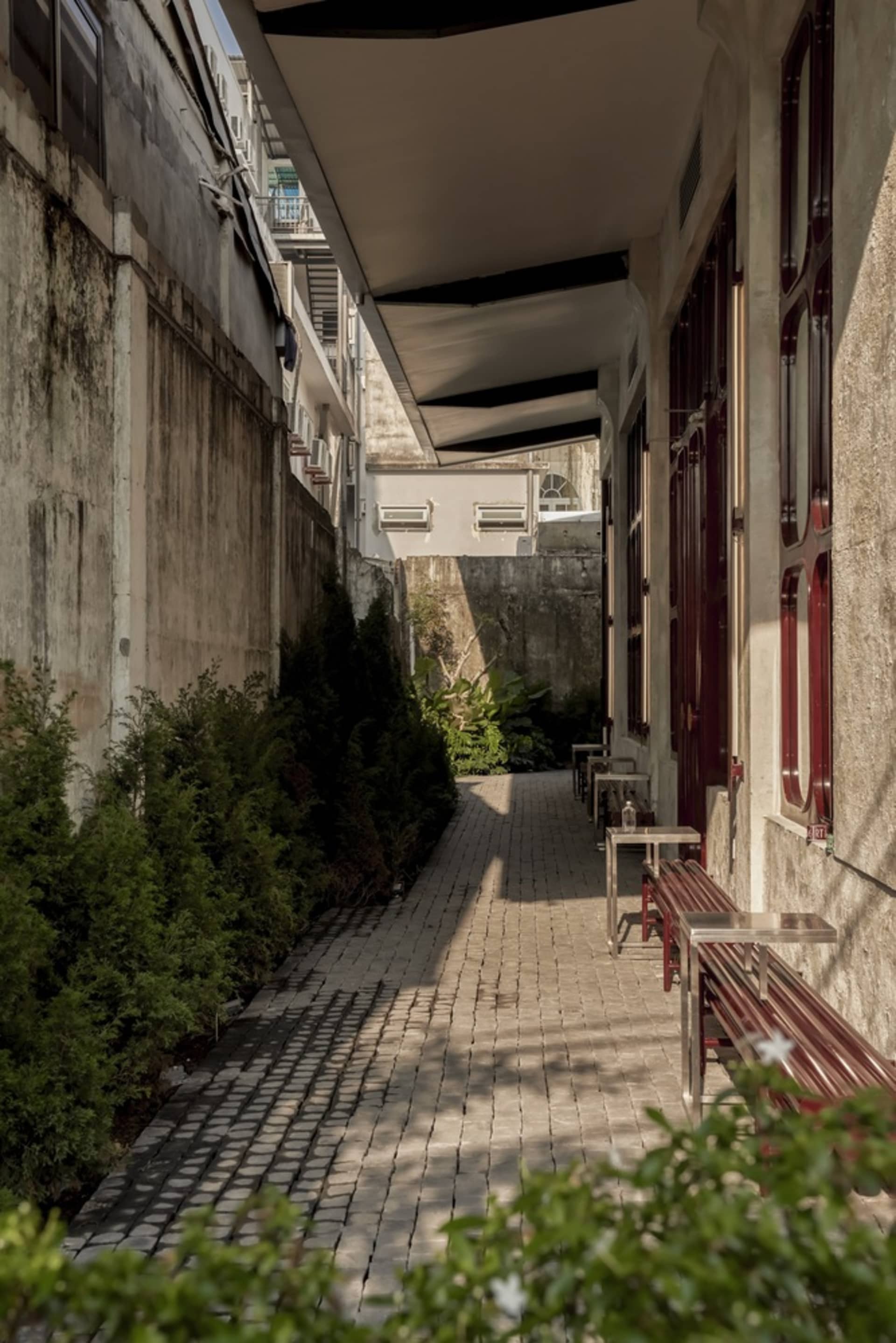An empty urban alleyway lined with brick walls and concrete elements, featuring greenery and light fixtures.