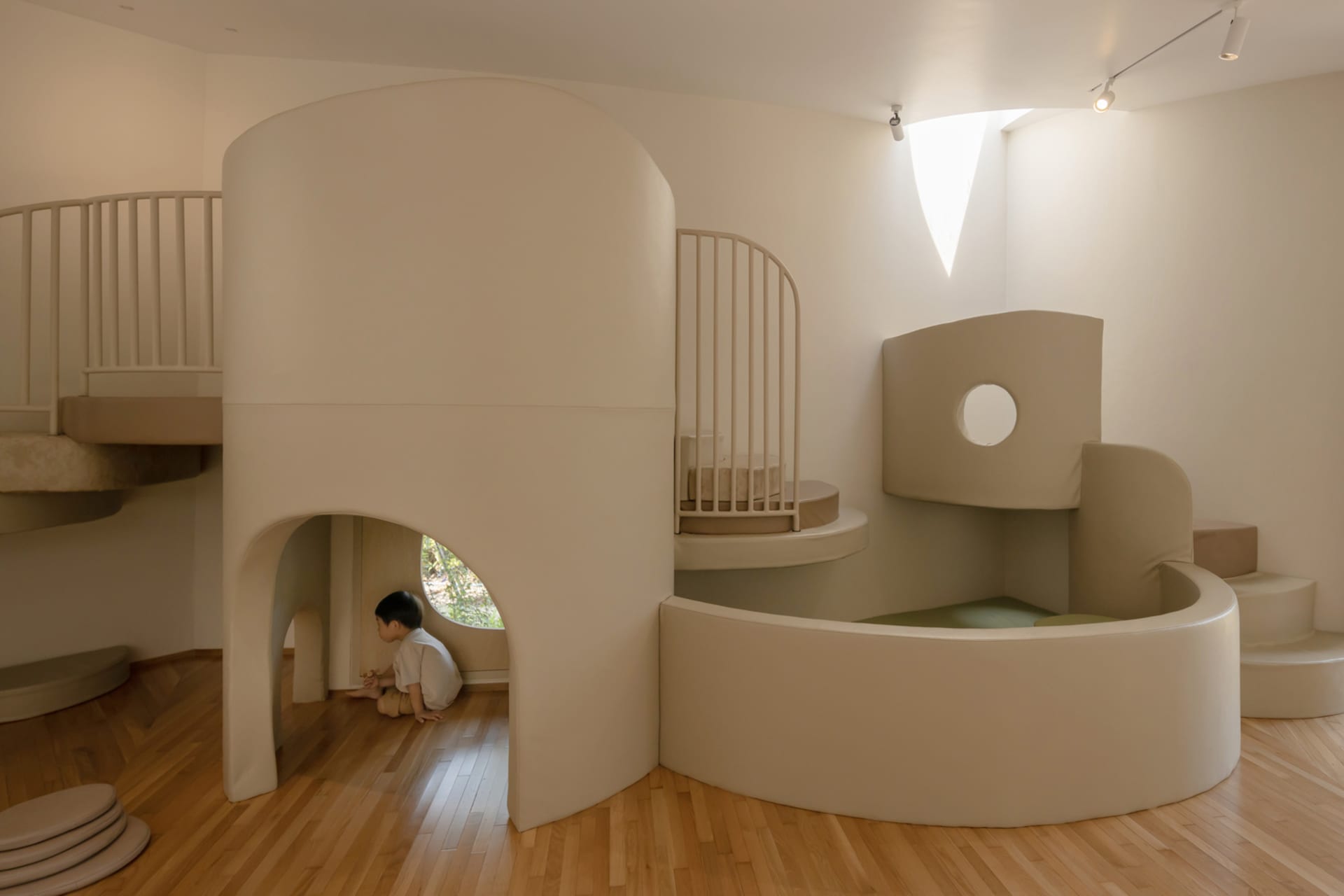 A modern, white playhouse with curved foam architecture designed for children's play, featuring a small window and steps.