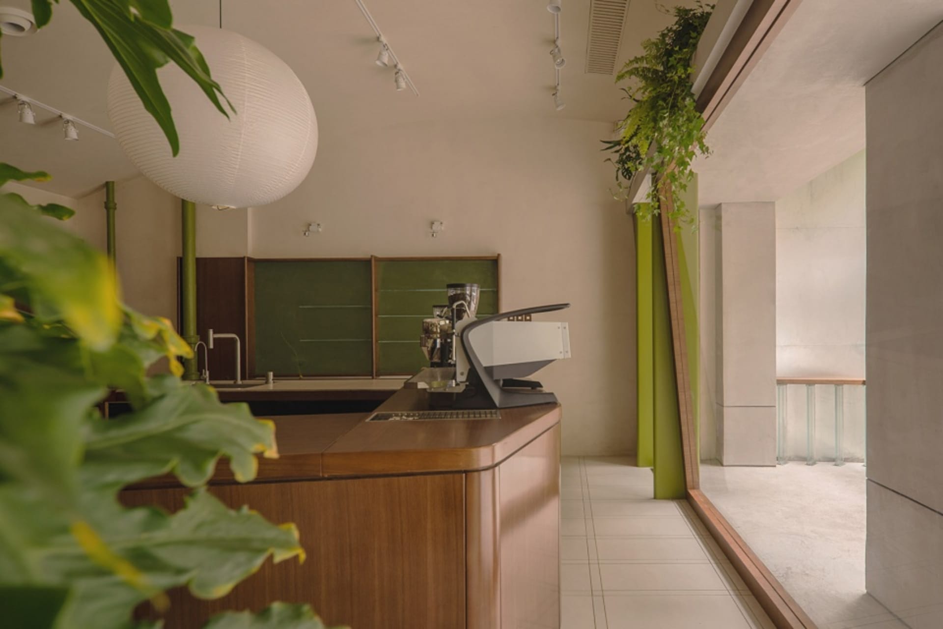 A modern coffee shop counter featuring wooden surfaces and green potted plants as part of its design