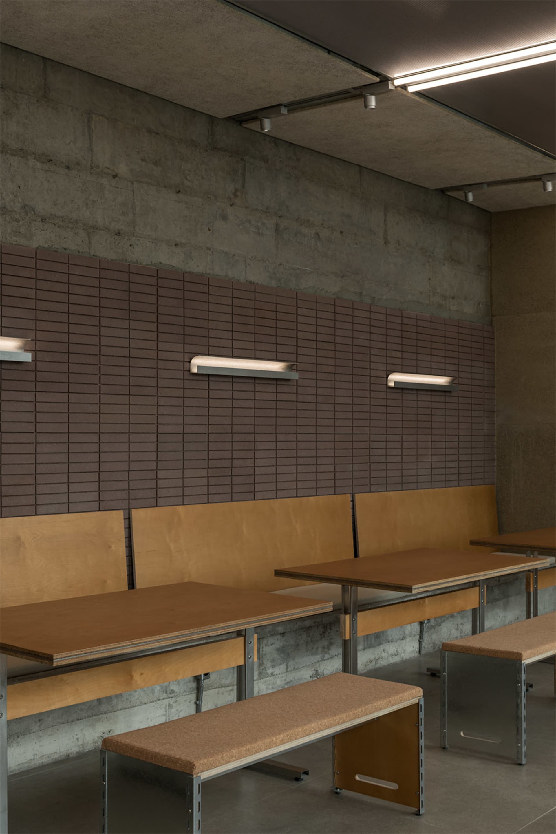 A modern classroom with concrete walls, wooden tables, and brown brick tiles on the lower half of the walls.