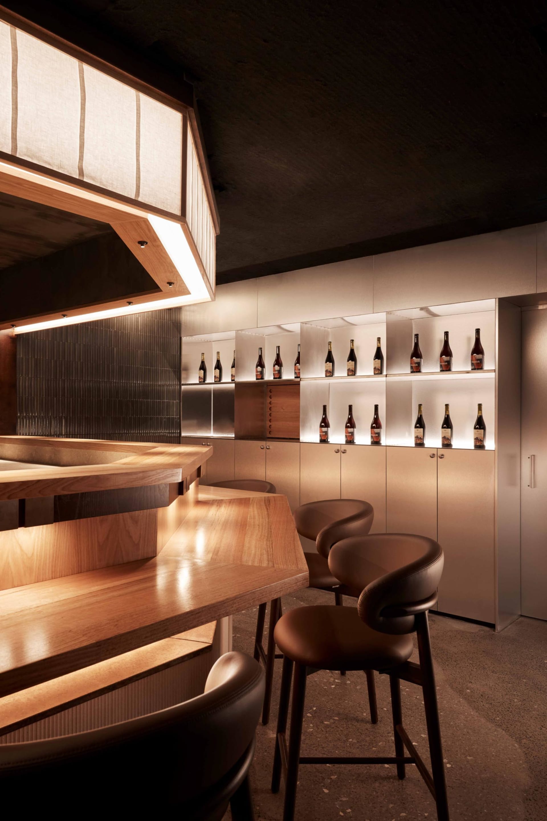 Contemporary bar interior with wooden counter and stools, showcasing modern design elements and materials.