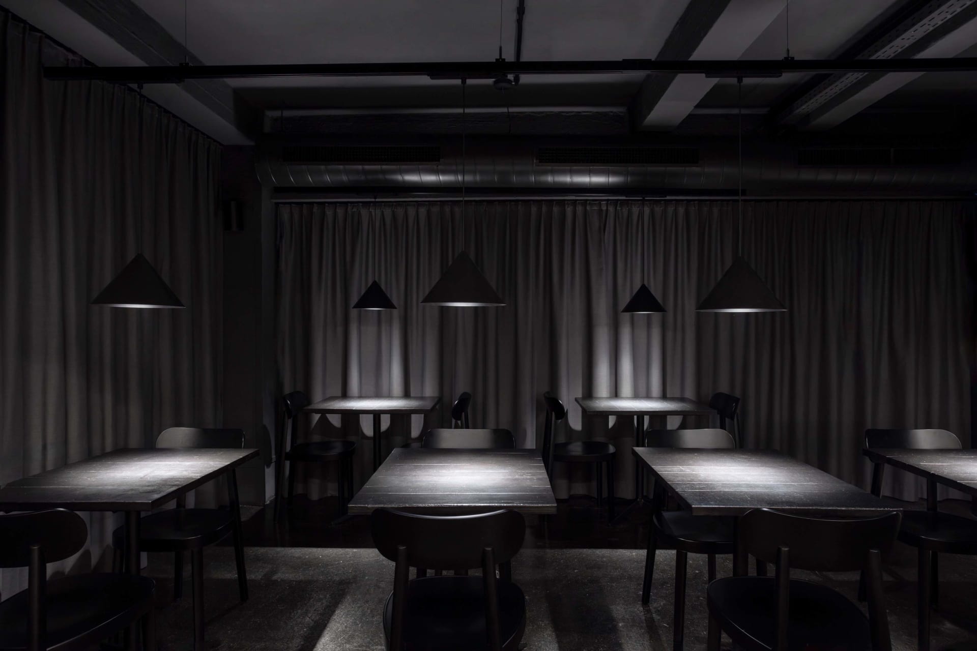 An empty minimalist-style restaurant interior with metal pendant lights and wooden tables.