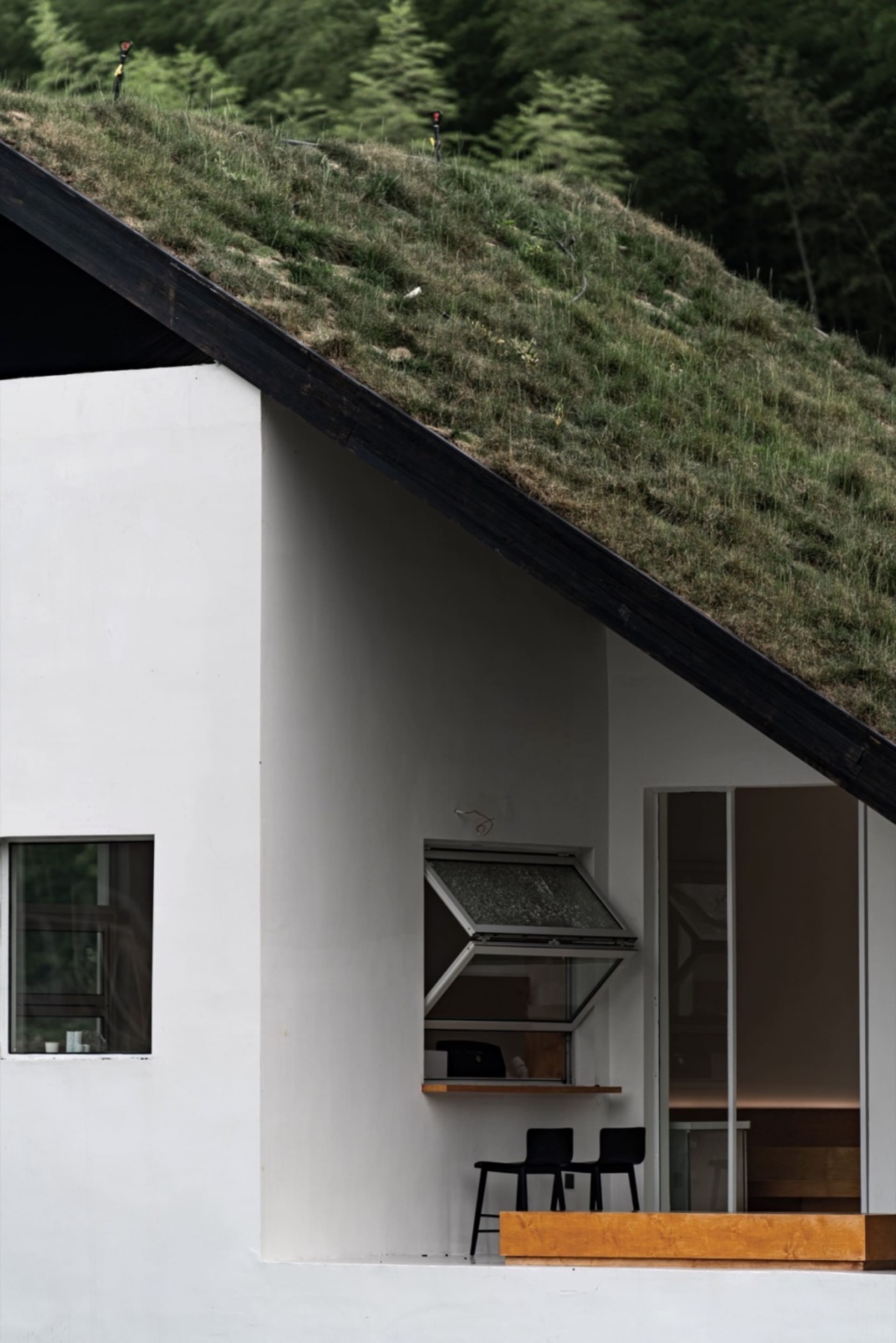 Modern minimalist white stucco house with a green grass-covered roof and contemporary black furniture on the porch.