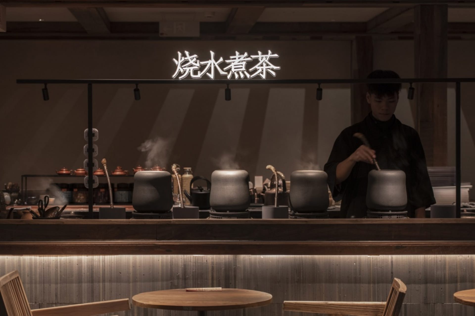 A dark, industrial-style coffee shop with wooden furniture and steaming tea kettles.