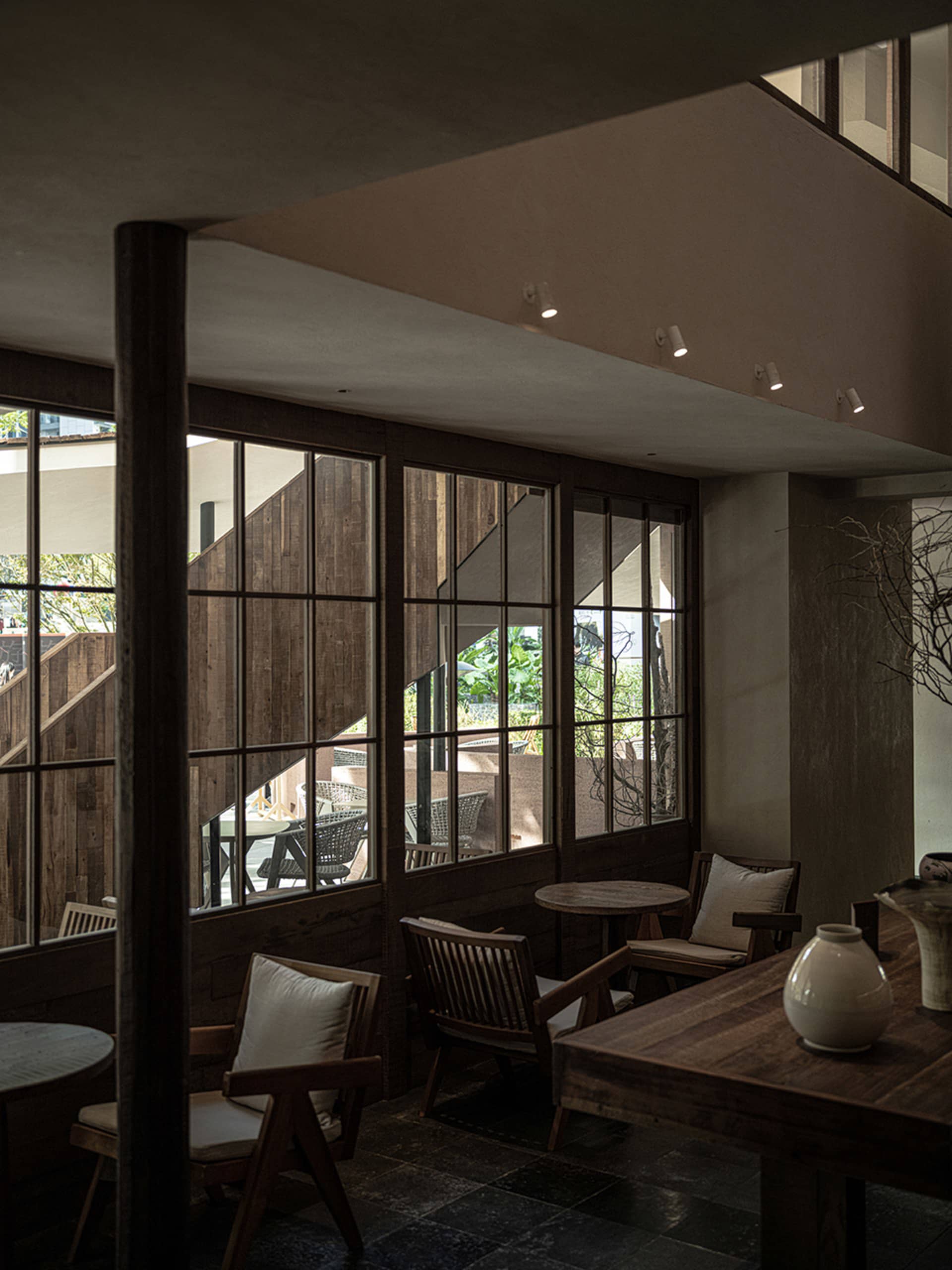 An indoor space with industrial design featuring wooden furniture and walls, glass windows, and comfortable seating options.