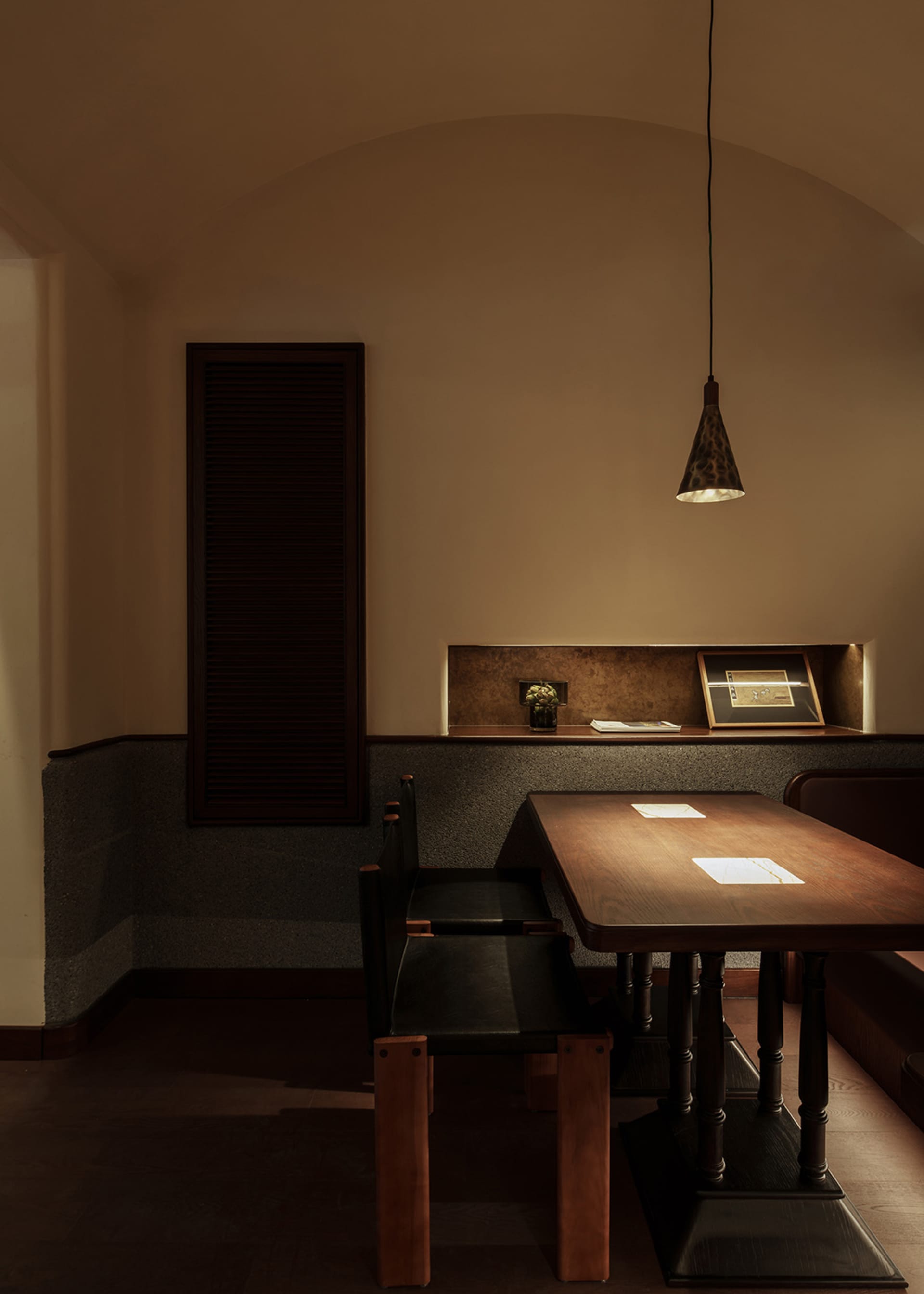 An industrial-style restaurant dining area with a wooden table, black leather chairs, and pendant lighting.