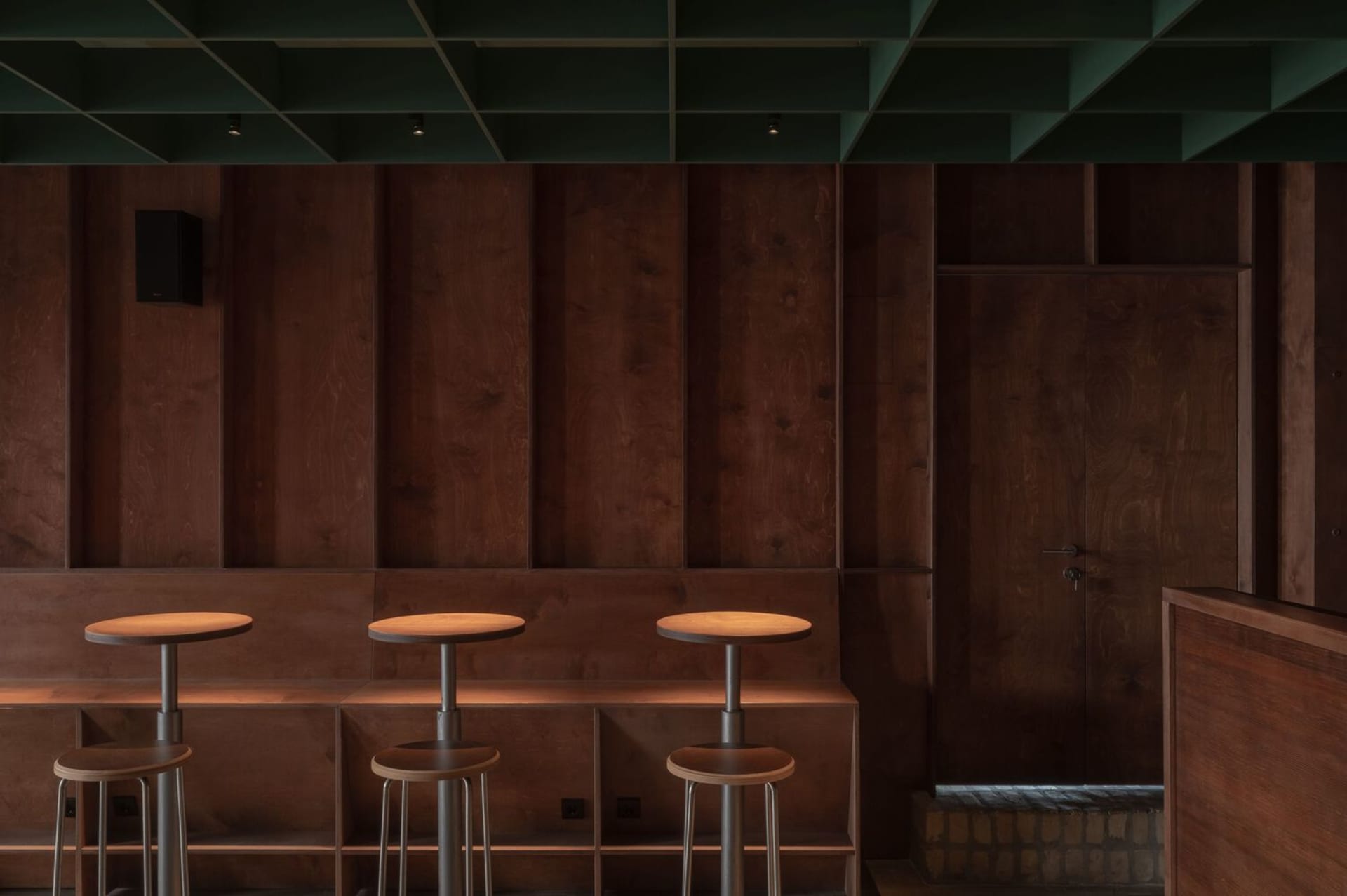 A minimalist bar area with a modern design featuring wooden and metallic surfaces and industrial stools.