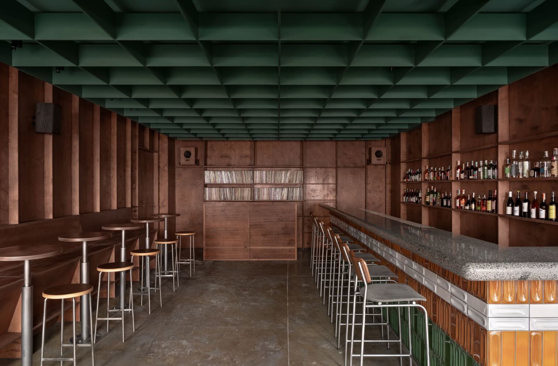 Concrete and wood interior of an industrial-style bar with high stools and shelves.