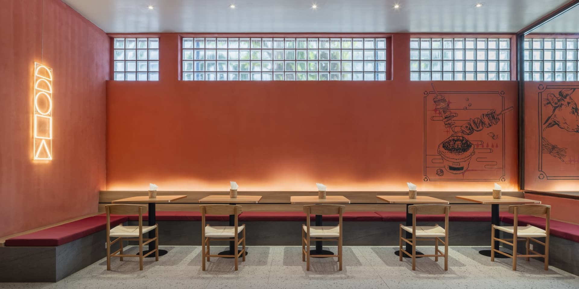 A modern restaurant interior with concrete walls, glass block windows, and wooden tables and chairs.