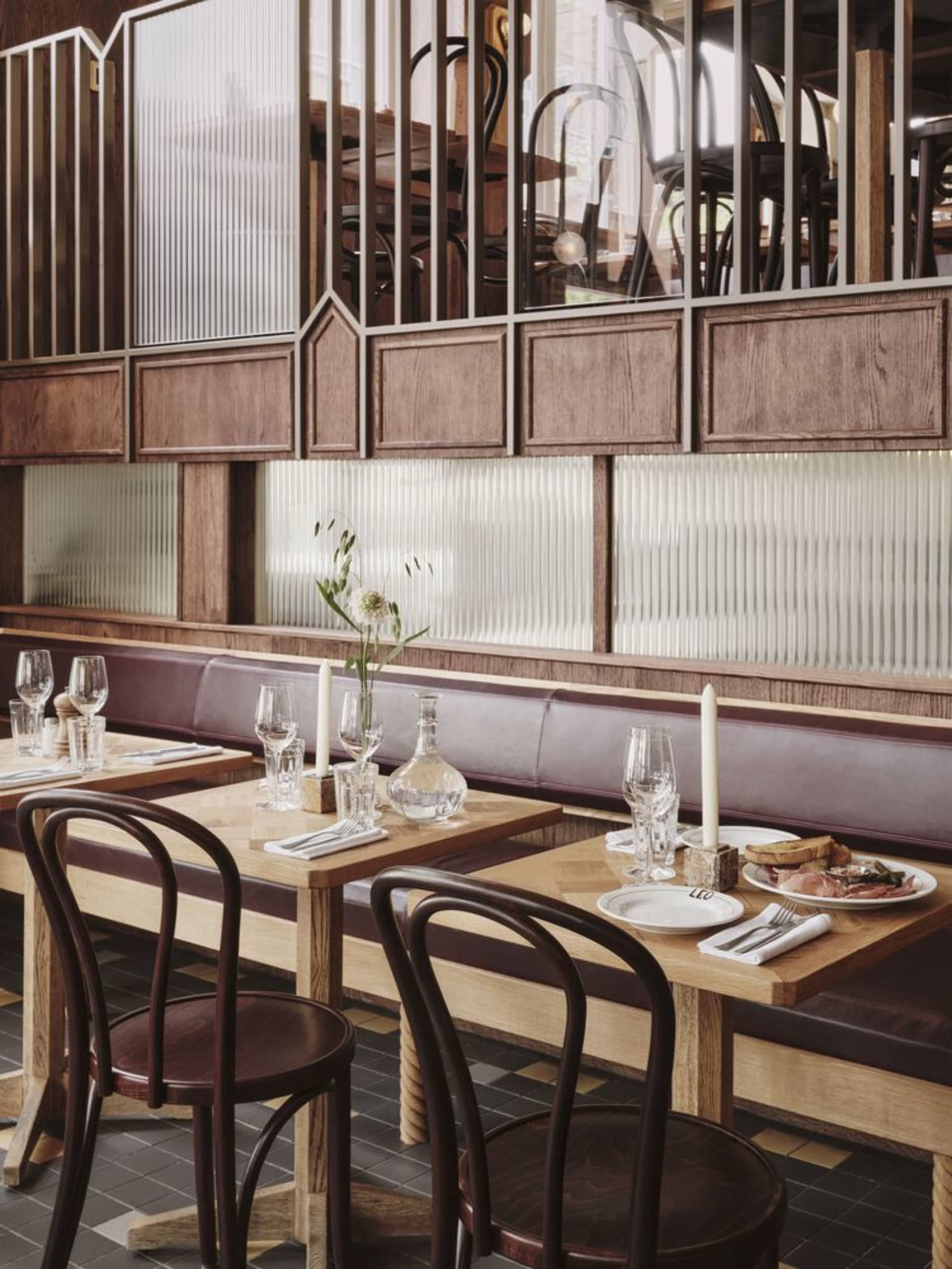 A modern restaurant interior with wooden tables, glass panels, and leather seating.