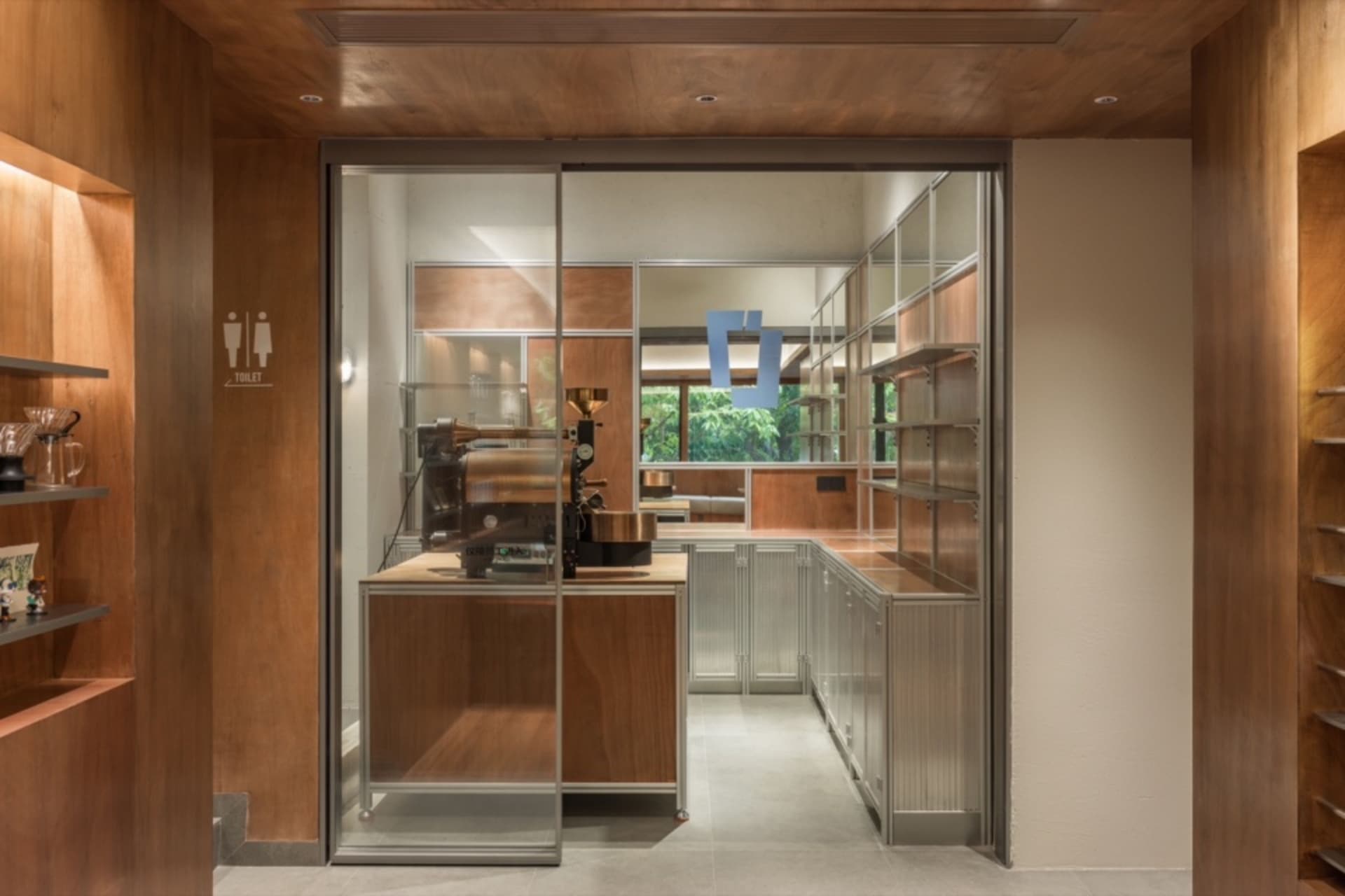 A modern coffee shop kitchen featuring metal cabinets and a glass wall.