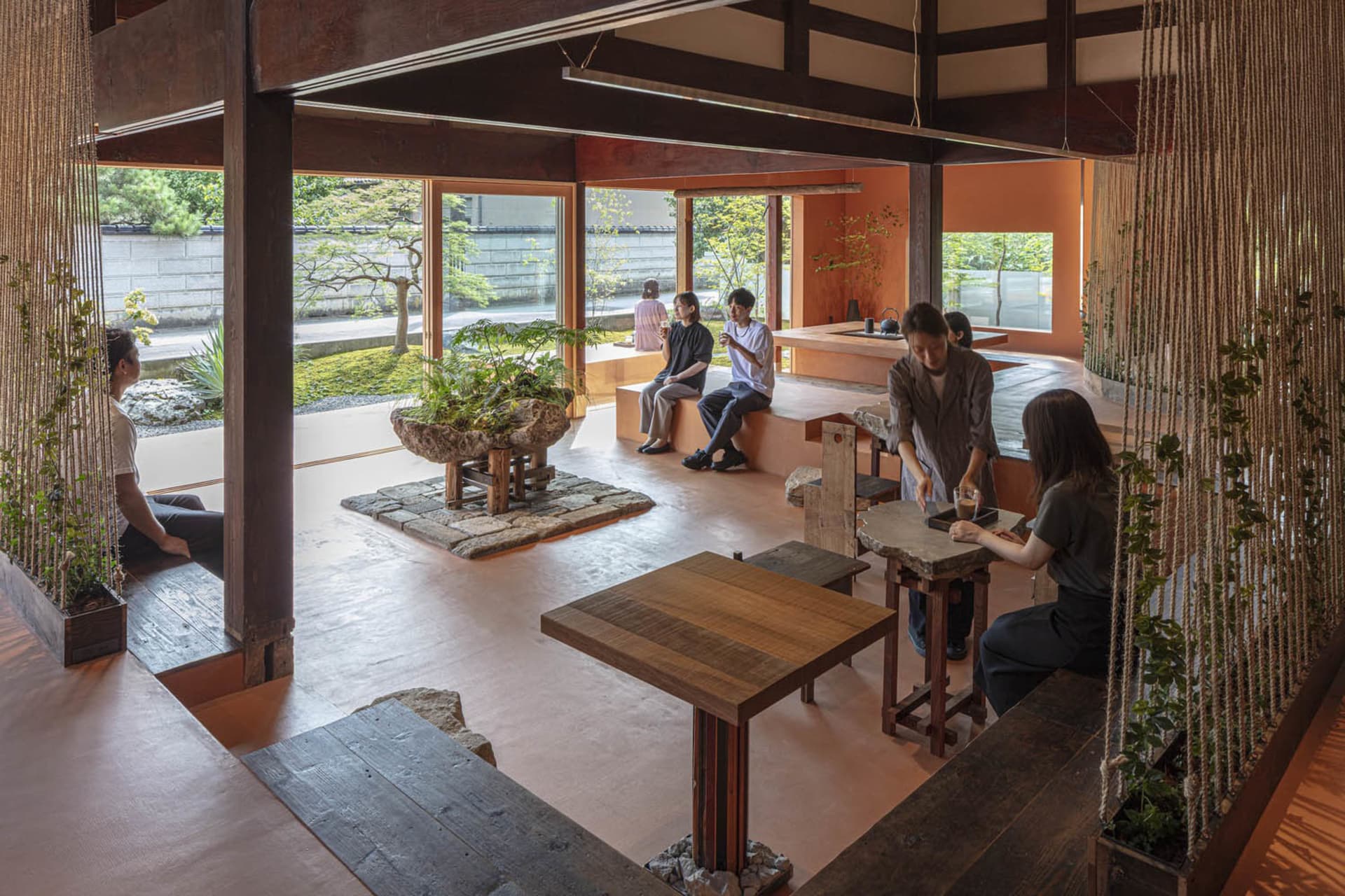 People enjoying a tea ceremony in a traditional Japanese tea house with wooden furniture and a natural garden view.