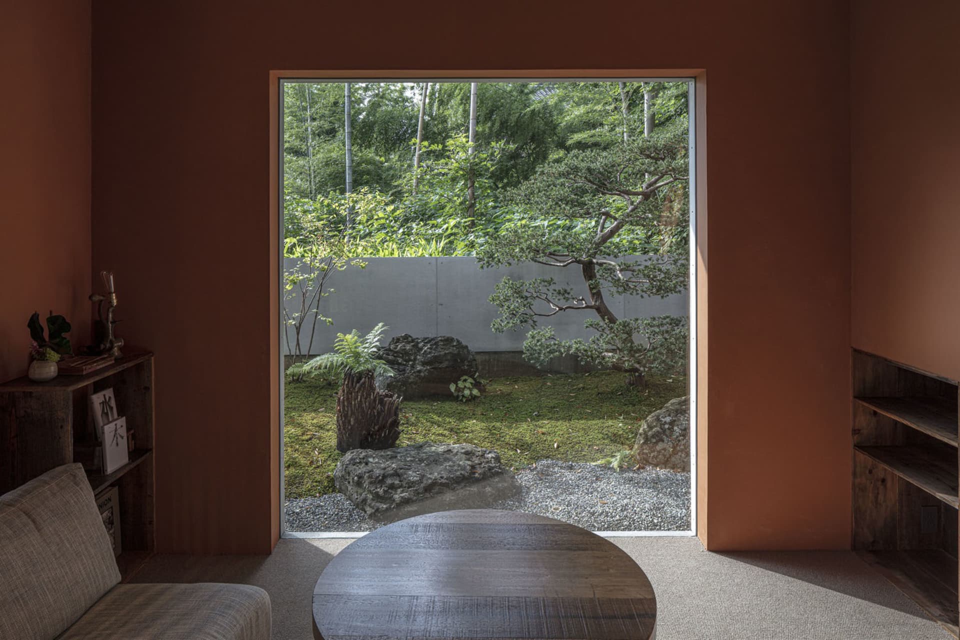 A serene modern interior featuring a gardenscape through a large window with stone, glass, and wooden elements.