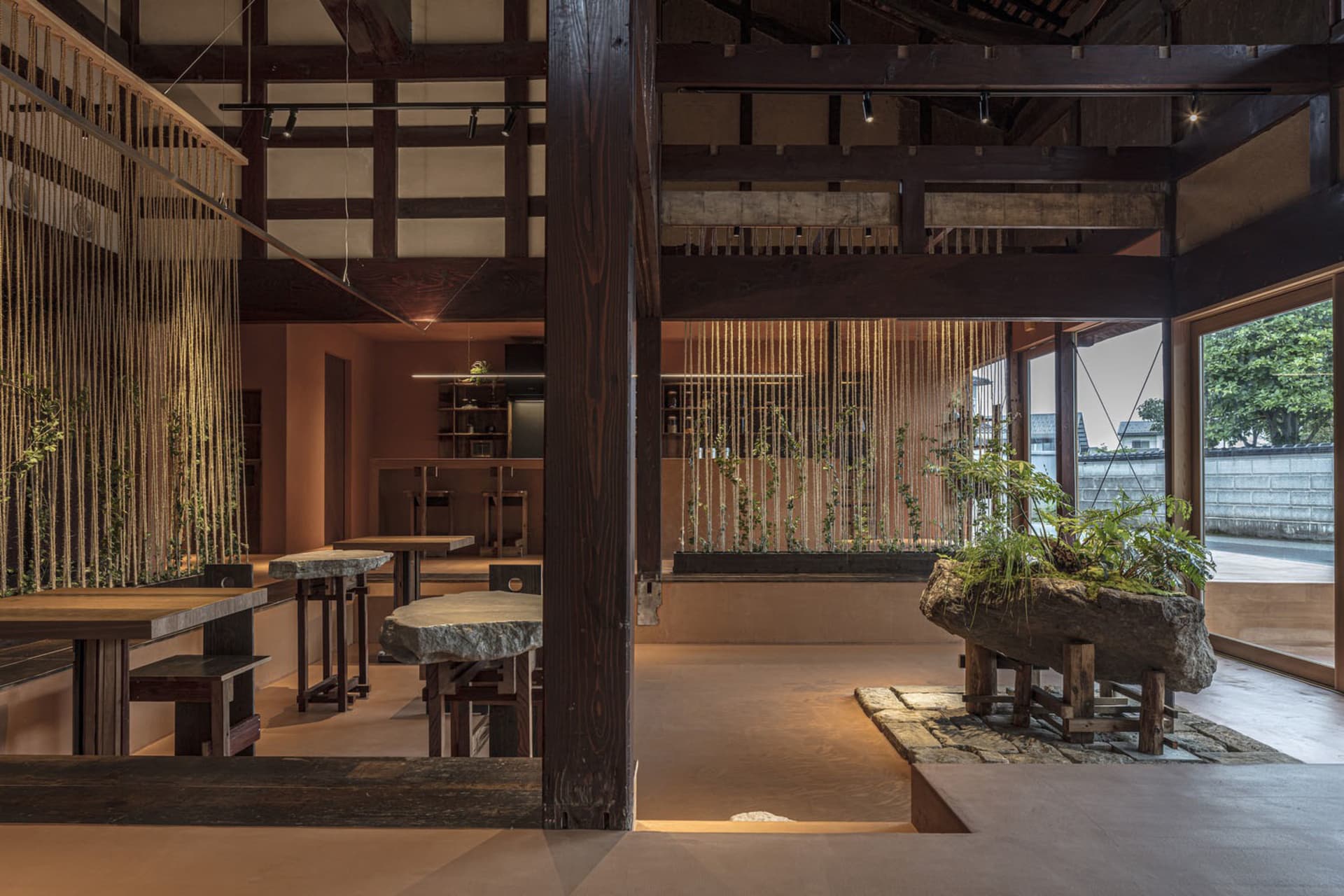 A spacious modern restaurant interior with wooden beams and tables adorned with plants.