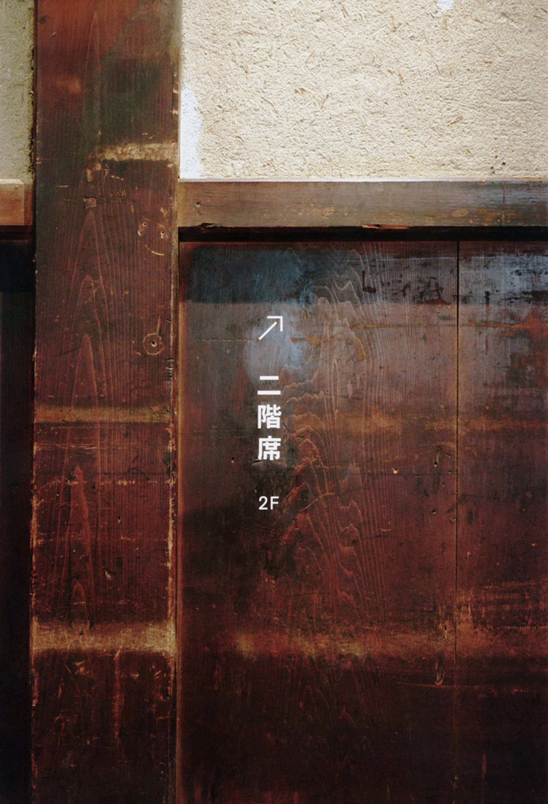 A wooden sign with Japanese text and an upward-pointing arrow.