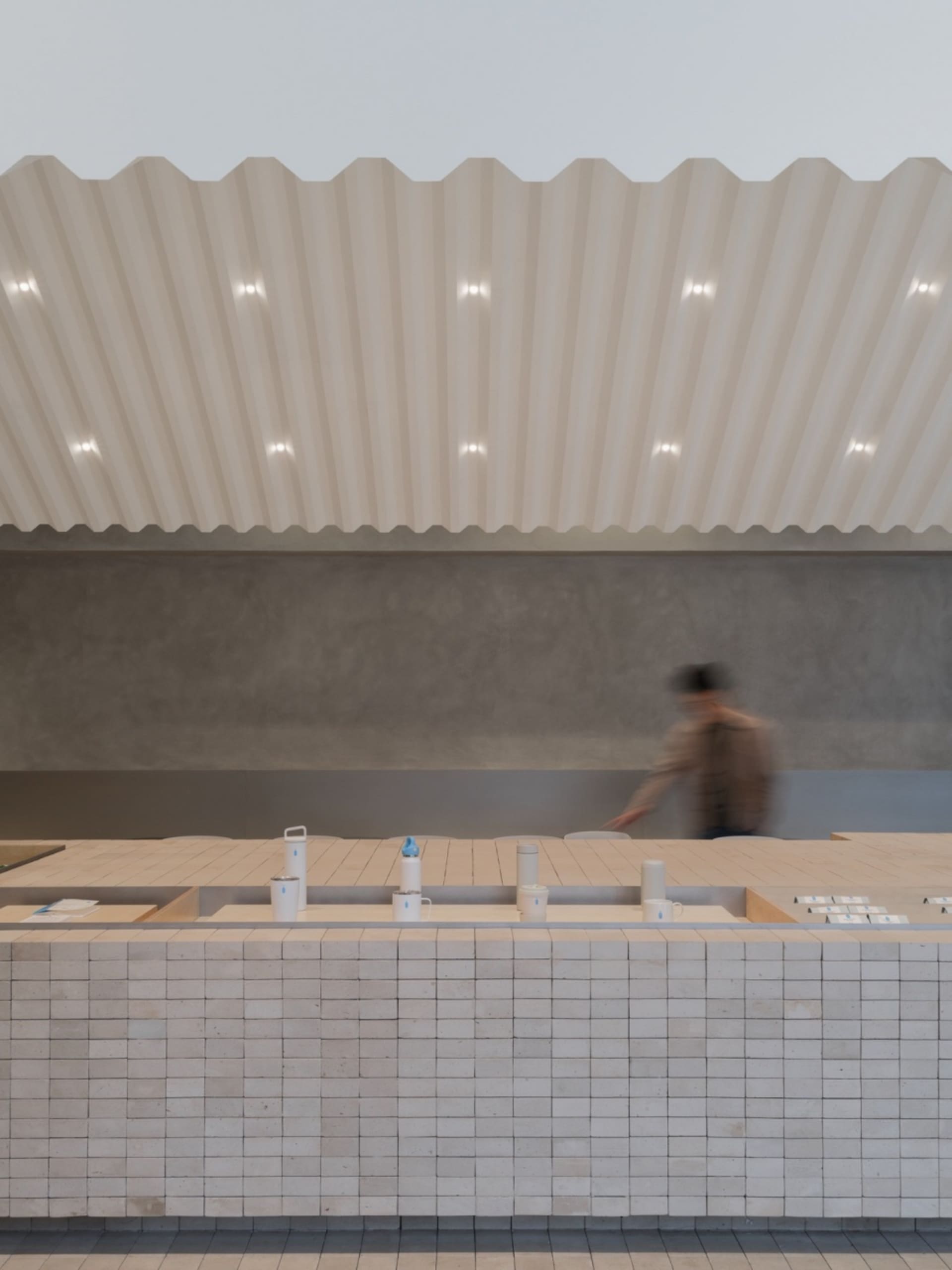A minimalist coffee shop interior with a tiled counter and a corrugated ceiling.