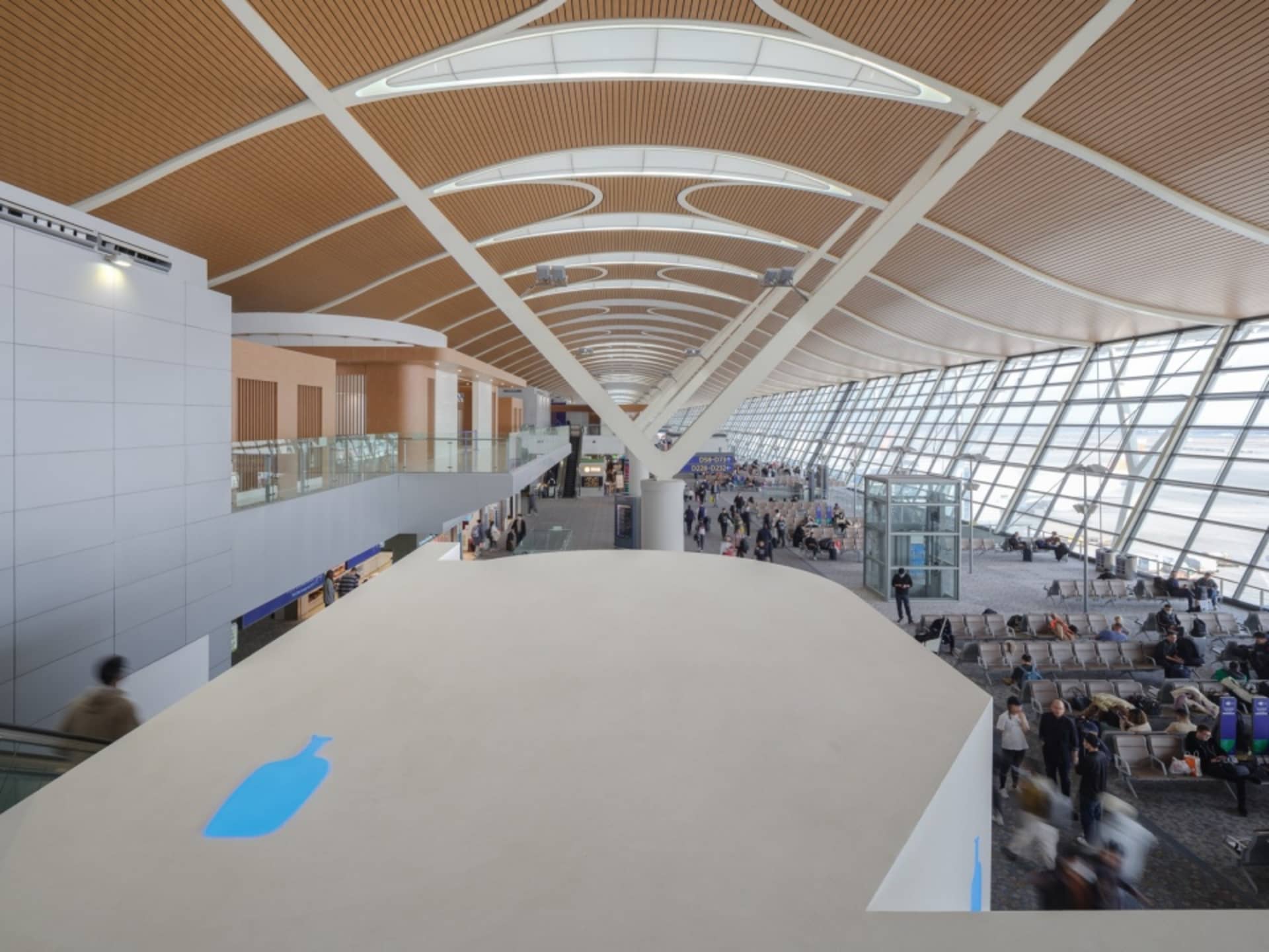 A spacious and modern airport terminal with a high, curved wooden ceiling adorned with circular lighting fixtures and expansi