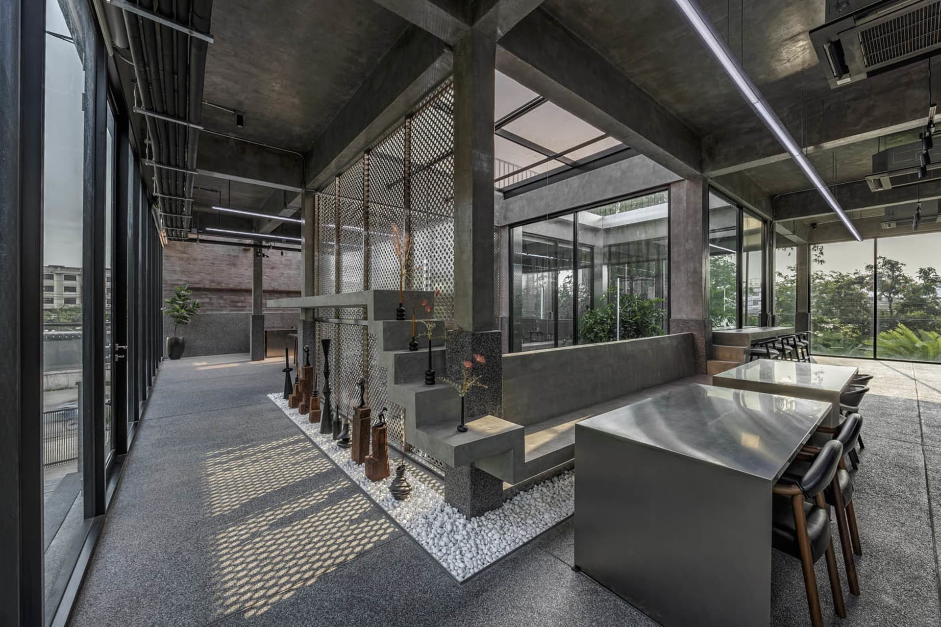 A modern industrial-style coffee bar with concrete walls and floor, featuring a metal table and chairs, and a glass partition