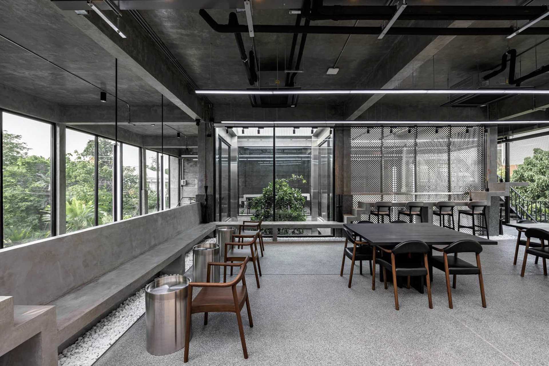 Industrial-style coffee shop with concrete walls and tables, featuring modern seating arrangements and ample natural light.