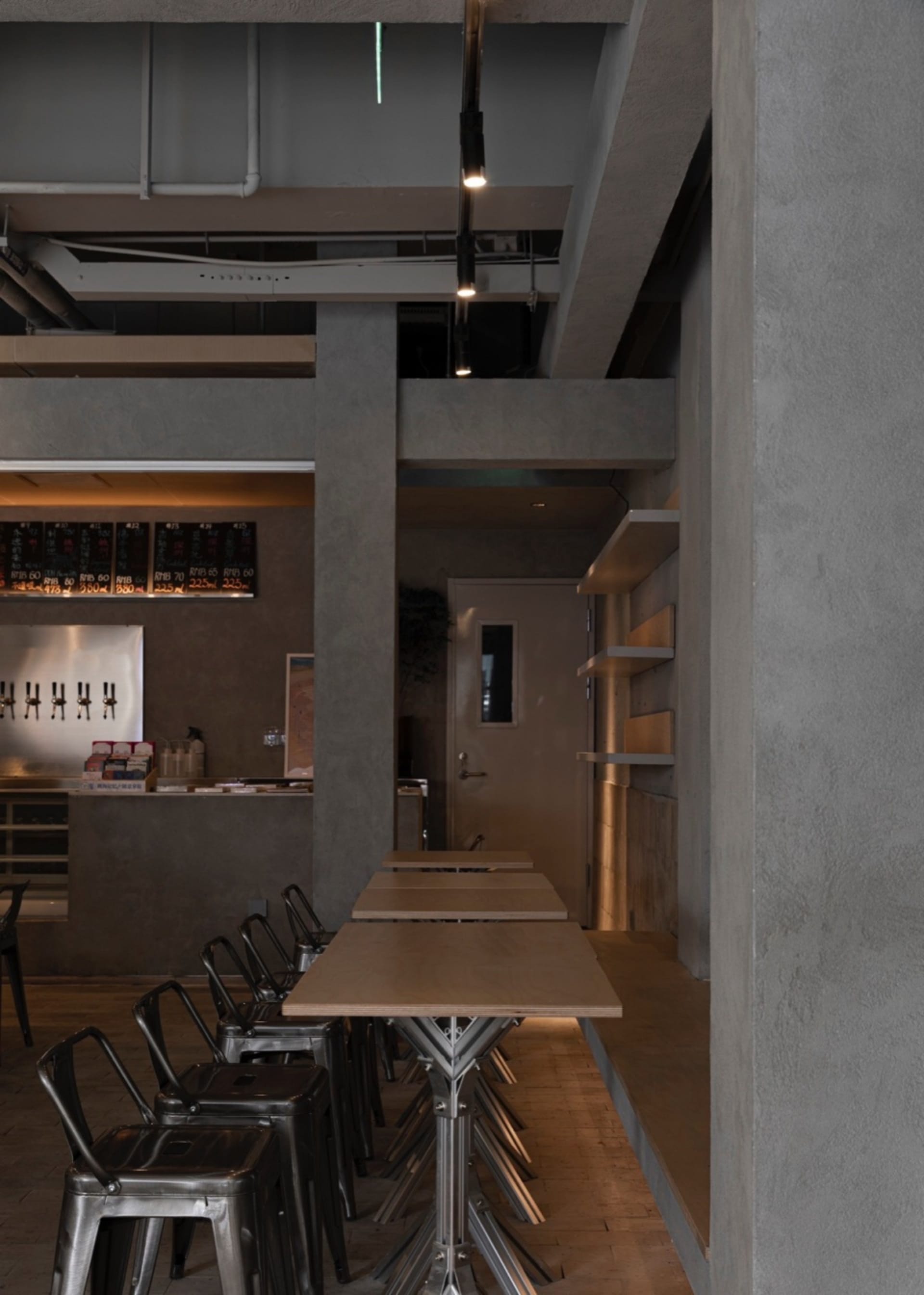 Industrial-themed restaurant interior with metal chairs, concrete pillars, brown wood elements, and white shelving.