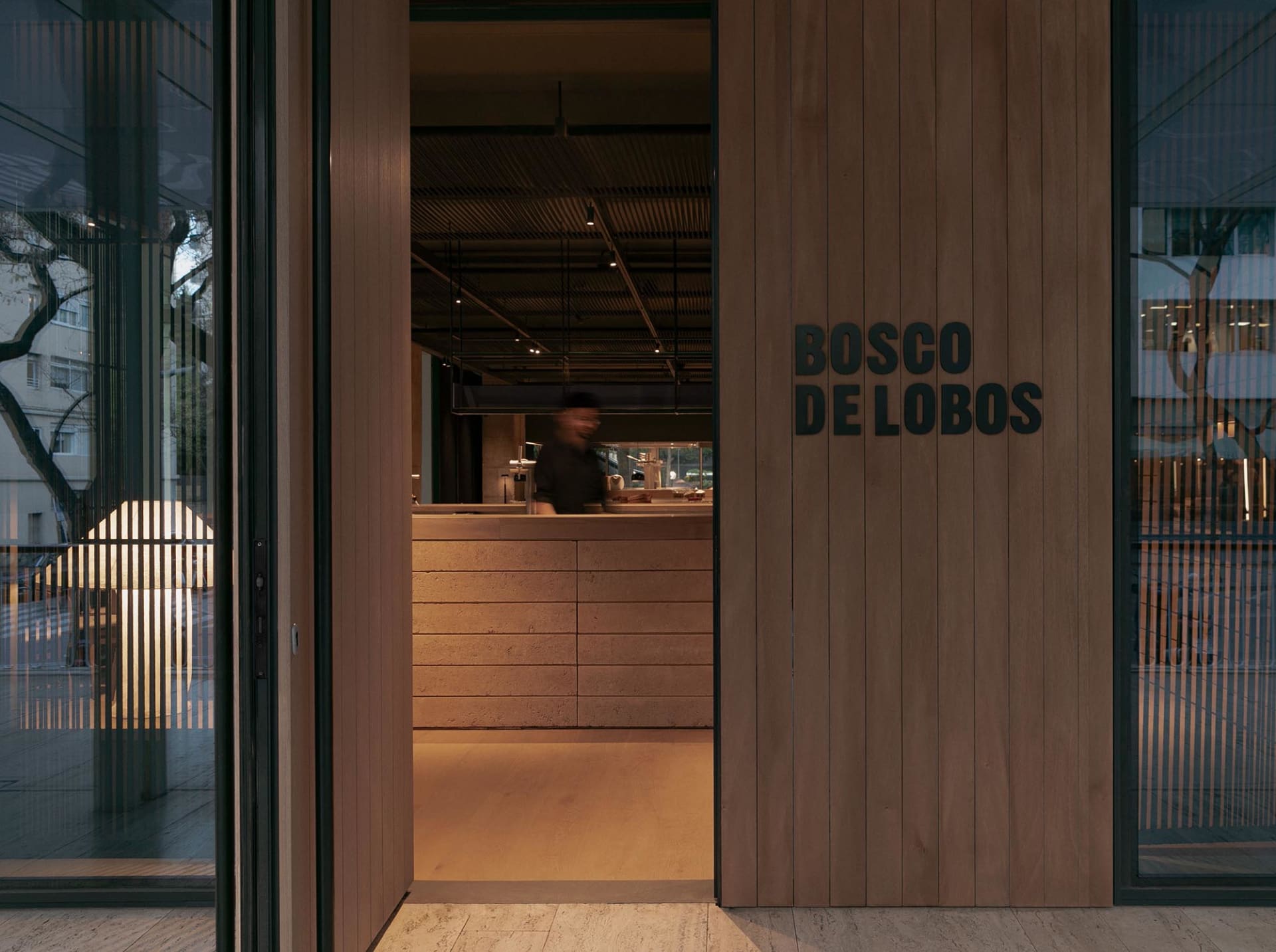 一扇帶有玻璃窗的木質板材門,門上寫著「BOSCO DE LOBOS」字樣,通往咖啡廳室內。