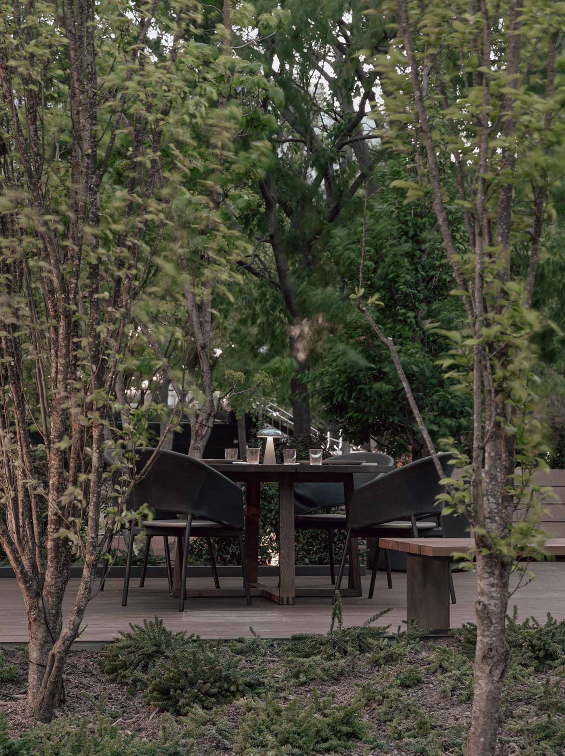 Modern outdoor dining area with wooden table, chairs, and greenery.