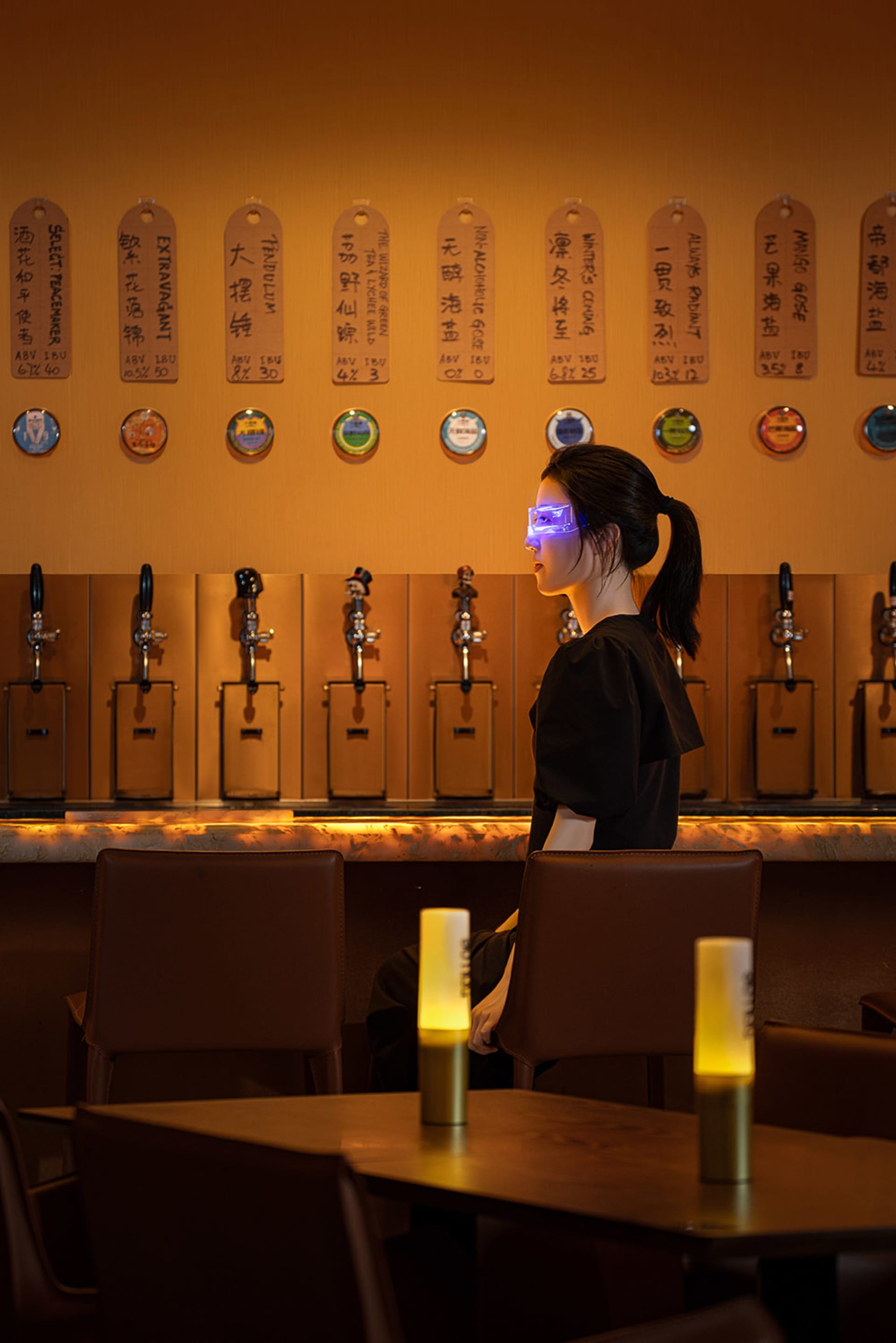 一位人士坐在燈光昏暗的餐酒吧內,搭配木製桌椅、皮革座椅、金屬啤酒龍頭與照明